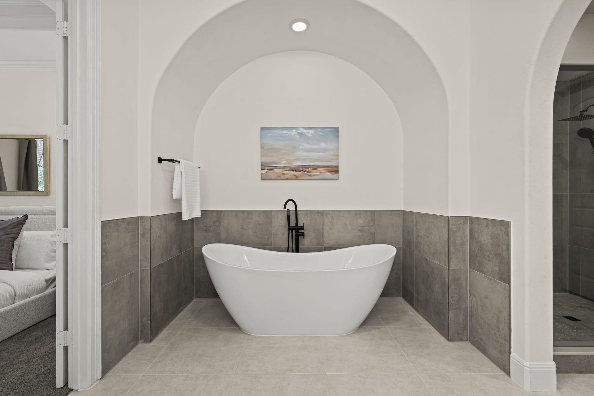 A freestanding soaking tub creates an elegant centerpiece within the renovated primary bathroom. Soft neutral tile and a graceful arched niche bring warmth and architectural interest.