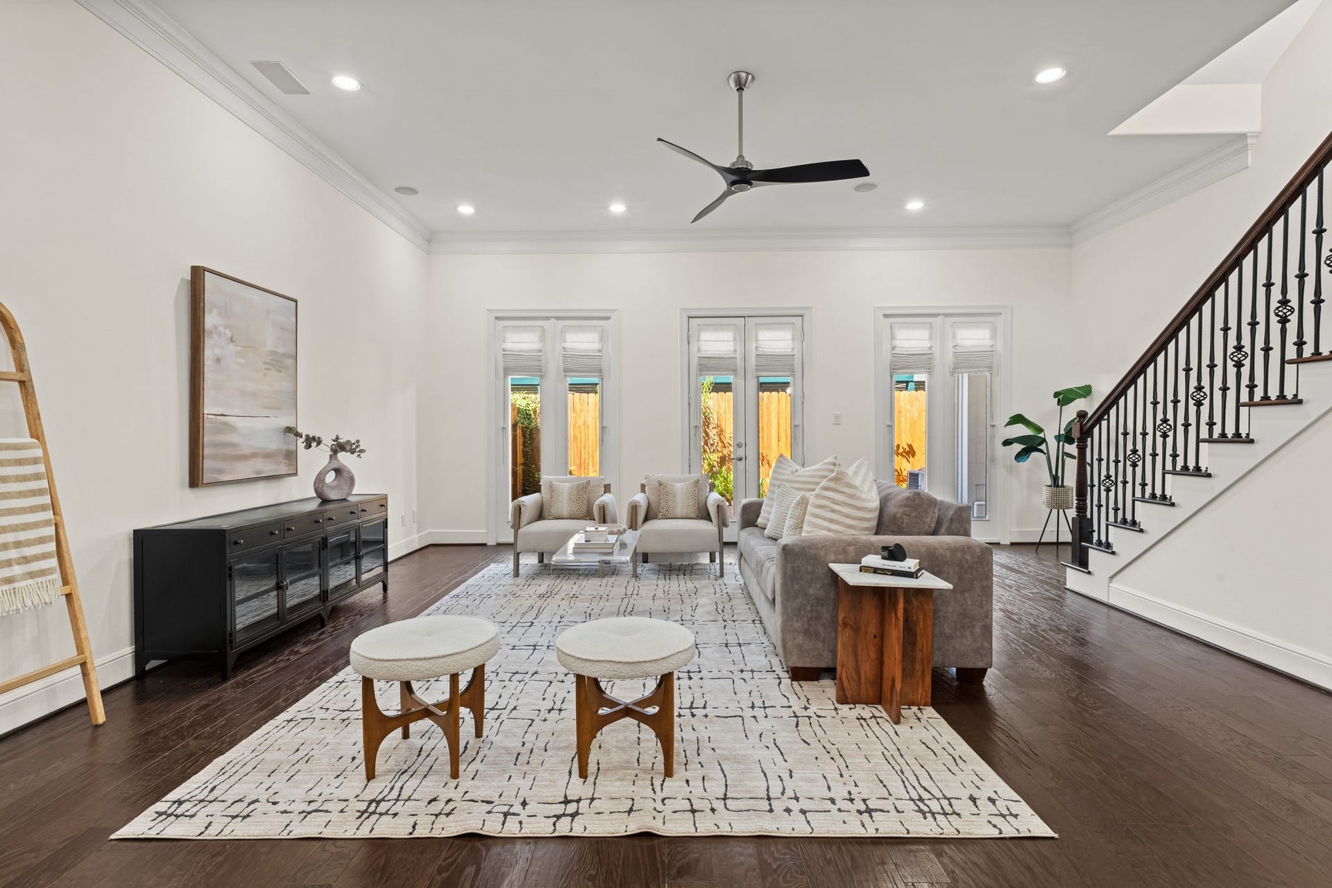 The spacious living room is brightened by tall glass doors and multiple windows. High ceilings, wood flooring, and an open layout create an airy environment for everyday living.
