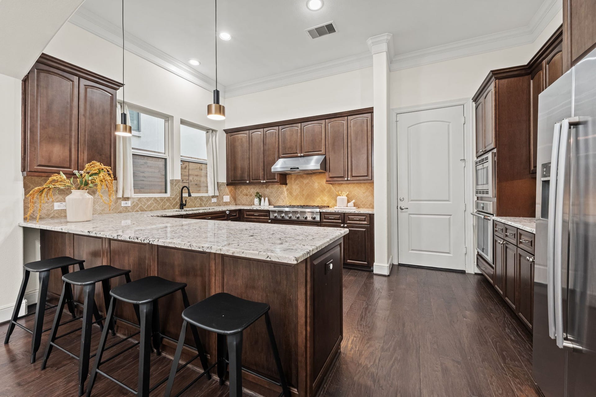 The kitchen combines timeless wood cabinetry with durable stone surfaces and stainless-steel appliances. An open arrangement keeps the chef connected to adjacent gathering spaces.