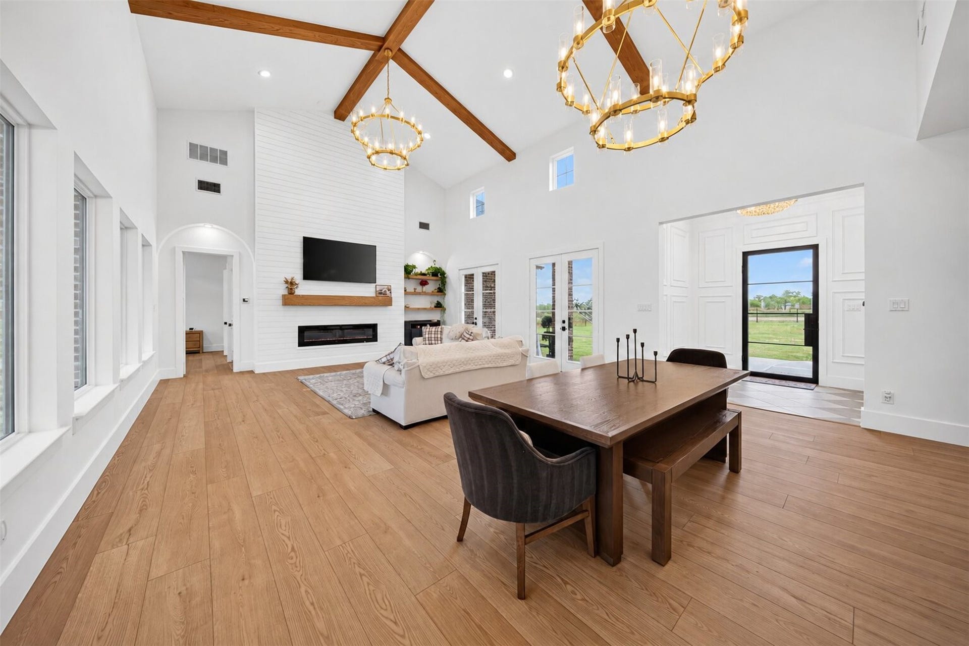 35851 Pineridge Road, Waller, TX 77484 Tall windows frame yard views across the open living and dining areas, unified by a vaulted ceiling and exposed wood beams.