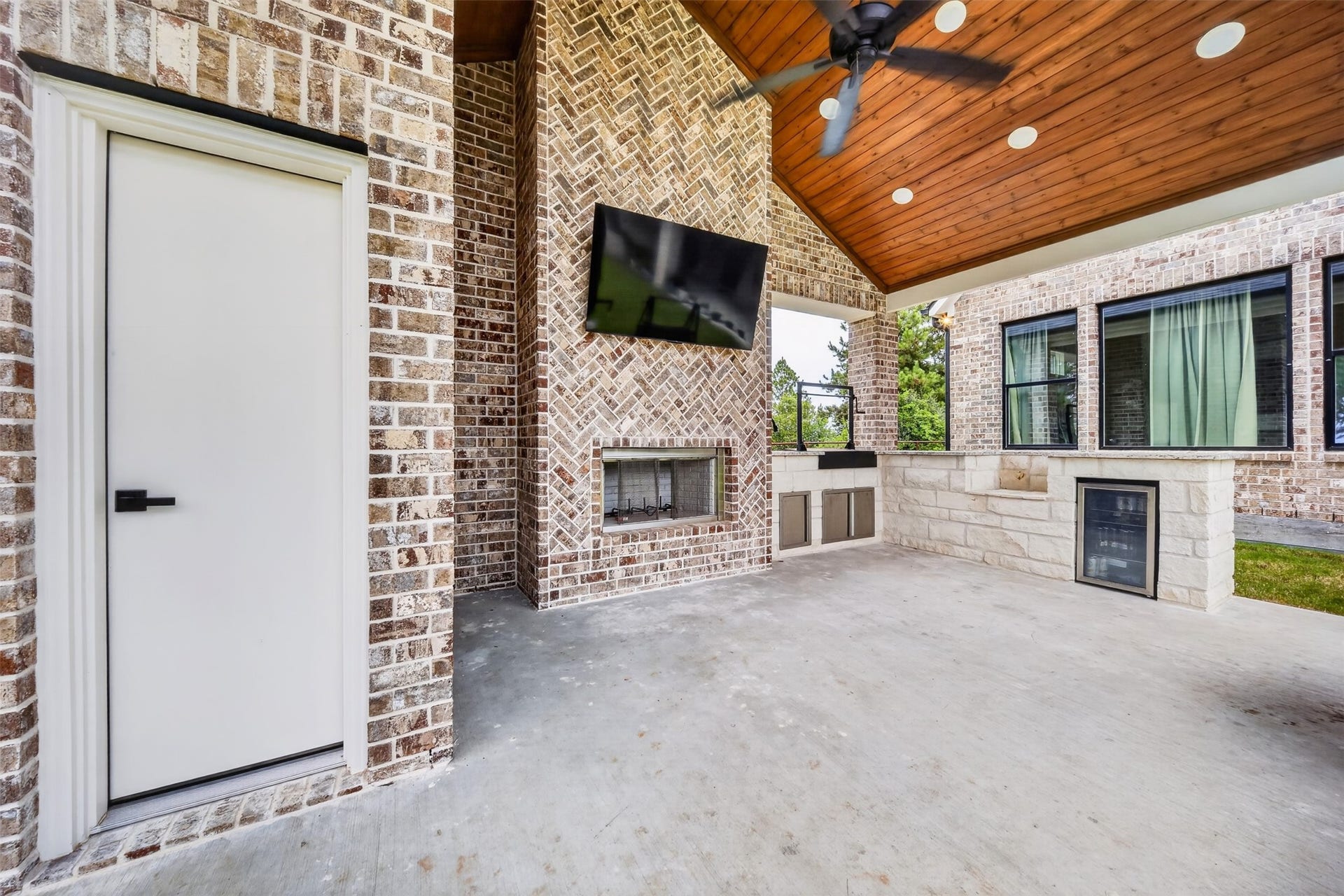 35851 Pineridge Road, Waller, TX 77484 The outdoor kitchen pairs stone counters with a brick fireplace wall, all sheltered beneath the covered patio's wood-plank ceiling.