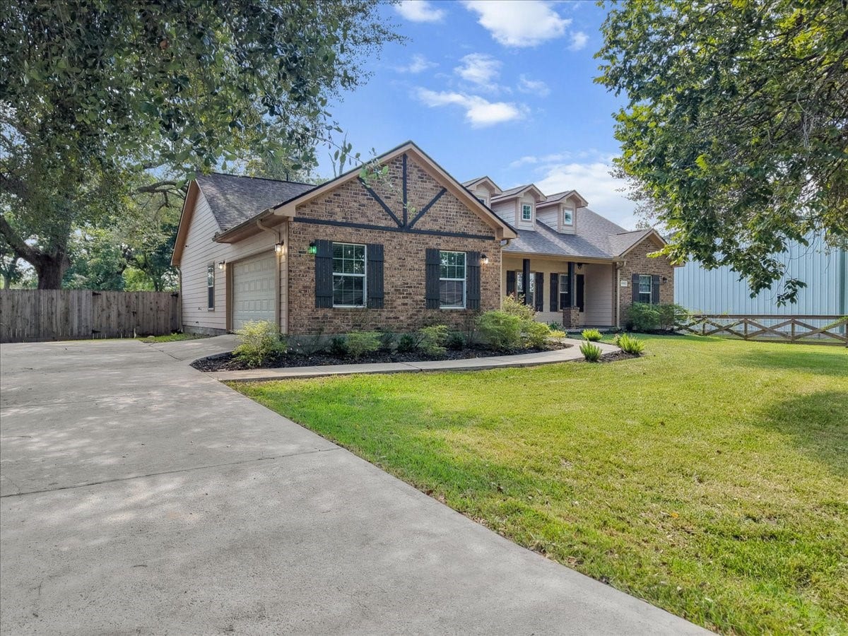 15531 Maple Street, Santa Fe, TX 77517 A generous double-wide driveway sweeps up beneath towering oaks, giving this brick craftsman-style home plenty of curb presence from the street. The open lawn and fenced side yard hint at the space and privacy that continue throughout the property.