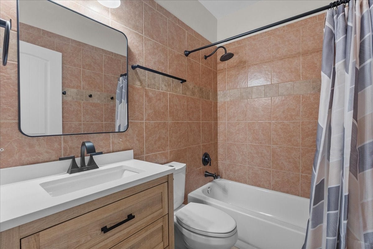 15531 Maple Street, Santa Fe, TX 77517 A full tub/shower combo is finished with floor-to-ceiling tile surround and a built-in towel bar, paired with a wood vanity topped in quartz and an updated matte-black faucet. A large framed mirror and overhead lighting complete the space.