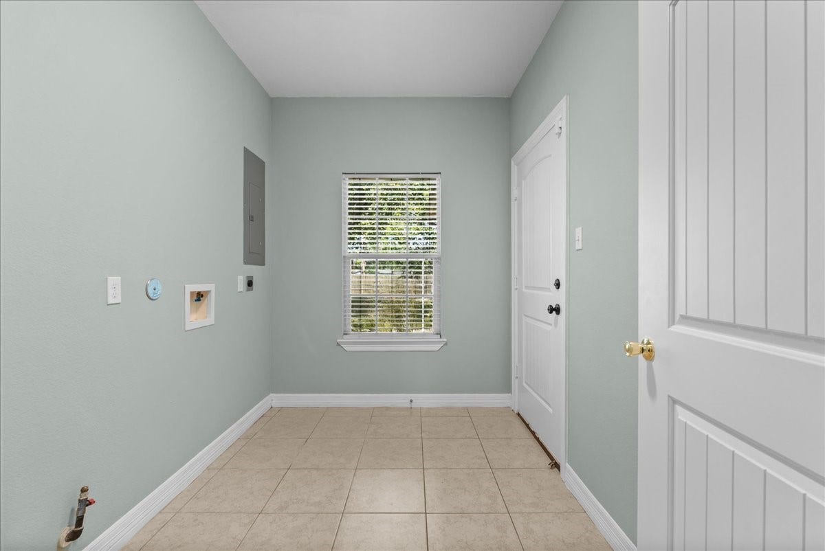 15531 Maple Street, Santa Fe, TX 77517 The spacious laundry room includes washer/dryer hookups, an electrical panel, and tile flooring, with a window bringing in natural light and a door leading out to the garage.