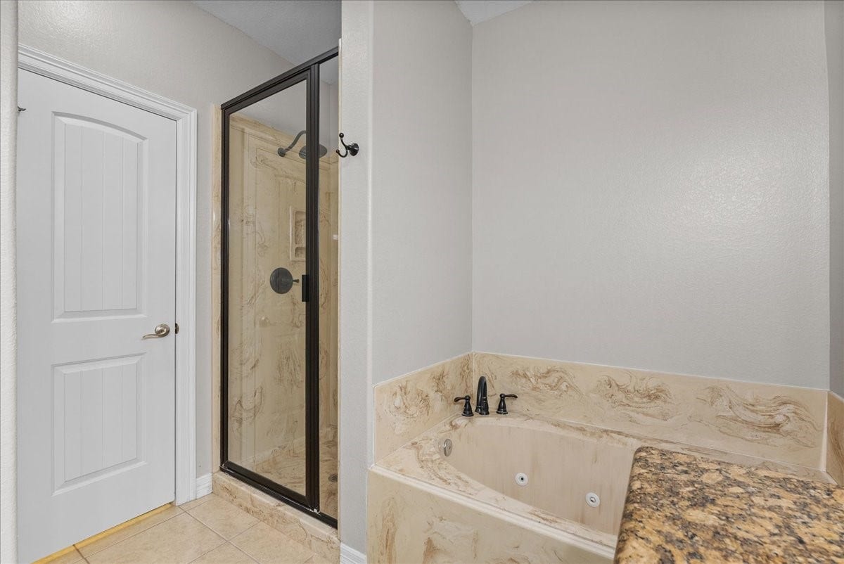 15531 Maple Street, Santa Fe, TX 77517 A frameless glass walk-in shower sits beside a separate garden tub with jets, both finished in coordinating marble-look surround. A private water closet door and granite countertop edge complete this spa-style ensuite.