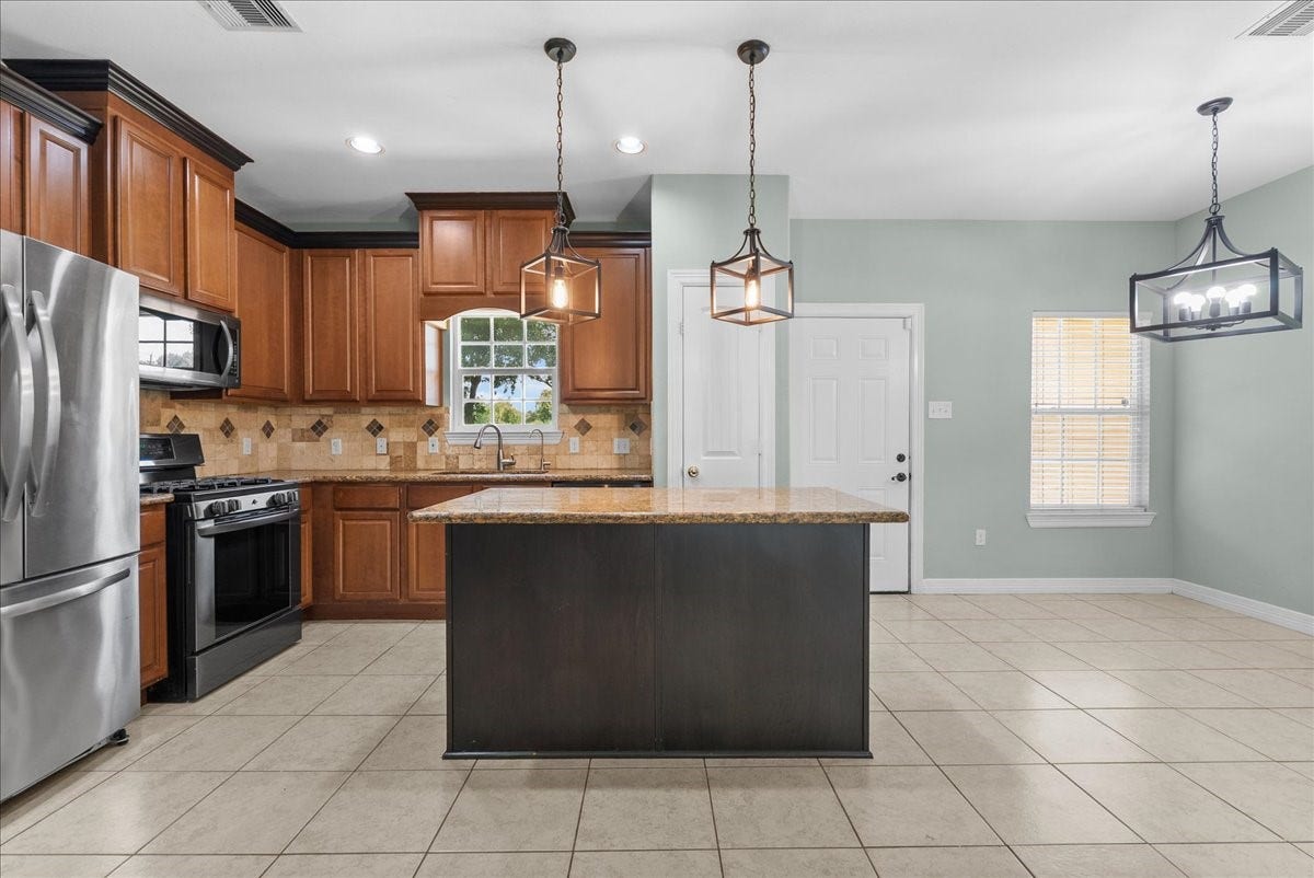 15531 Maple Street, Santa Fe, TX 77517 The kitchen is finished with granite counters, a tile backsplash, and a large center island with seating space, framed by three pendant lights overhead.