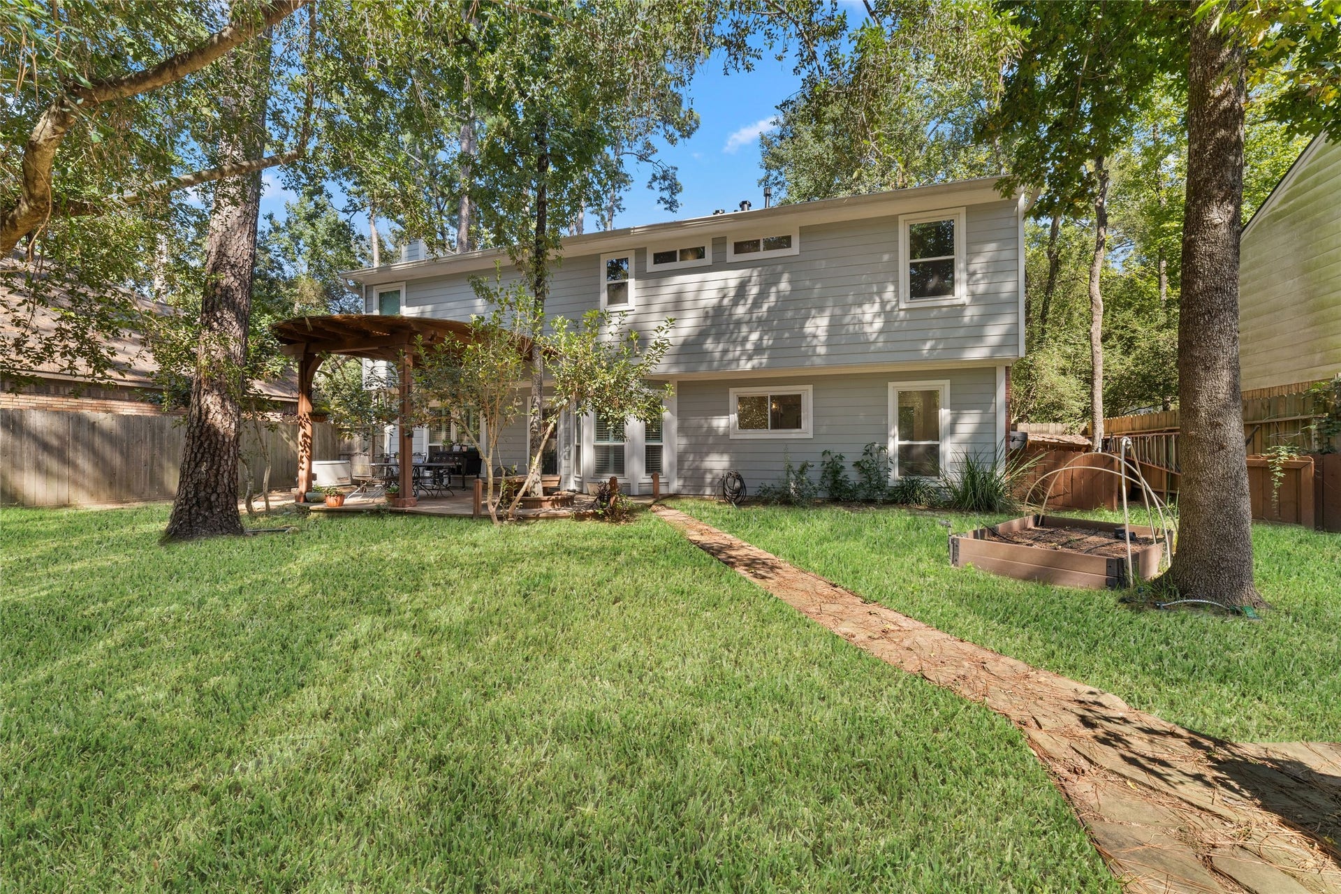 218 E Rainbow Ridge Circle, The Woodlands, TX 77381 Charming two-story home with a spacious backyard, featuring a cozy pergola, raised garden beds, and lush greenery, perfect for outdoor gatherings and relaxation.