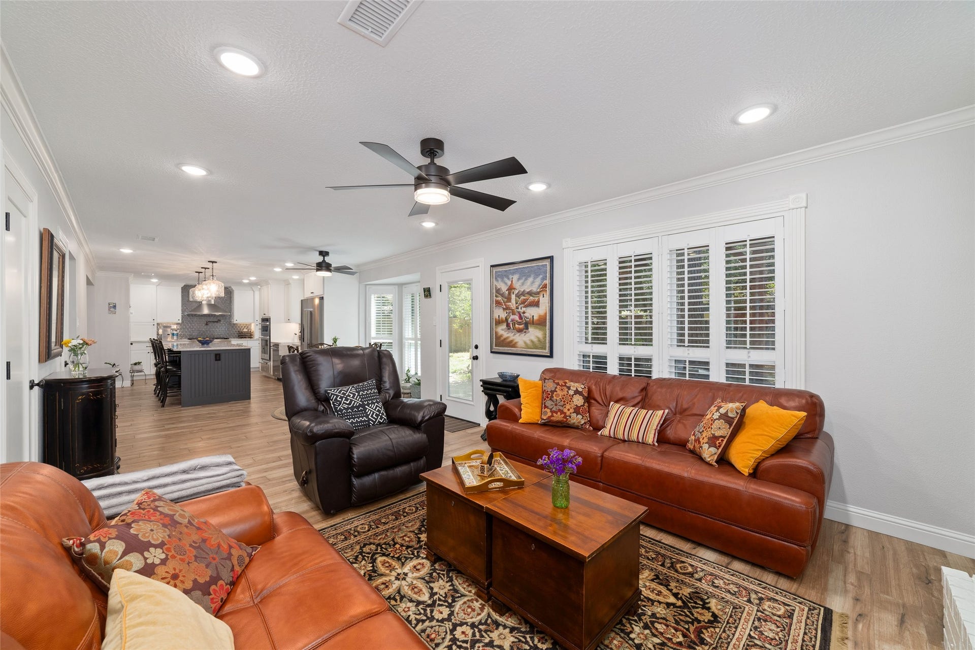 218 E Rainbow Ridge Circle, The Woodlands, TX 77381 Spacious living area with light, wood-look tile flooring, featuring modern ceiling fans, and abundant natural light through large windows with plantation shutters.