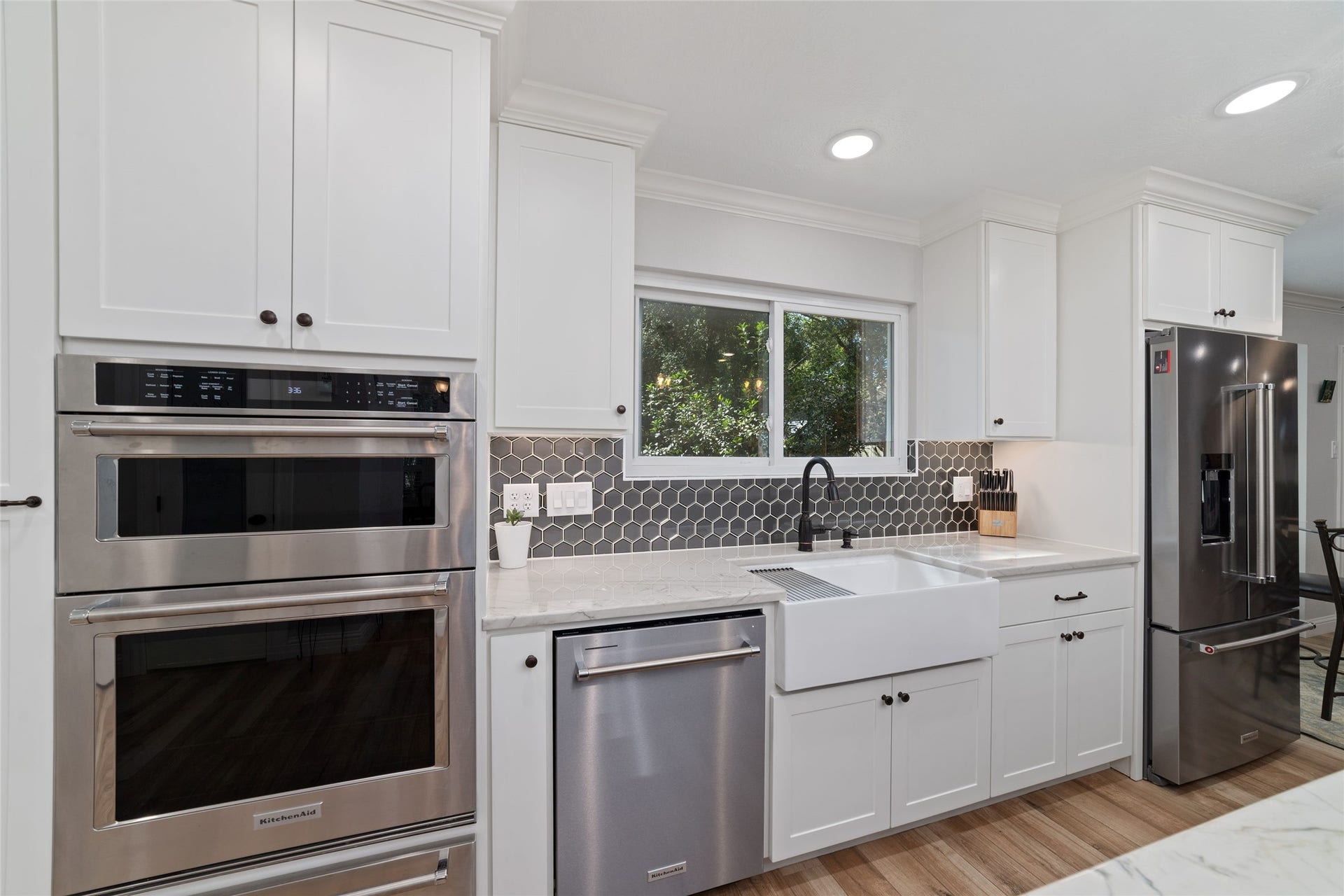 218 E Rainbow Ridge Circle, The Woodlands, TX 77381 Sleek kitchen featuring newer stainless steel appliances, a farmhouse sink, and elegant white Shaker-style cabinetry complete with floor-to-ceiling spice rack to left of oven.