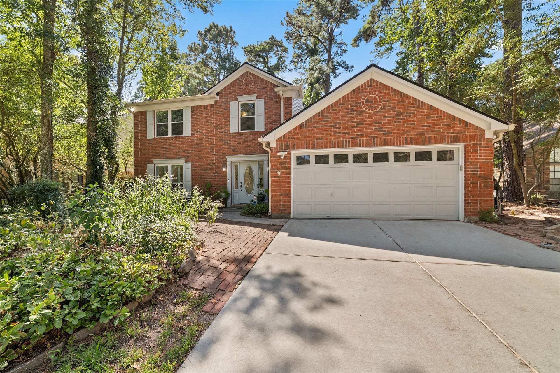 218 E Rainbow Ridge Circle, The Woodlands, TX 77381 Charming two-story brick home nestled among mature trees, featuring a spacious driveway and inviting front entrance.