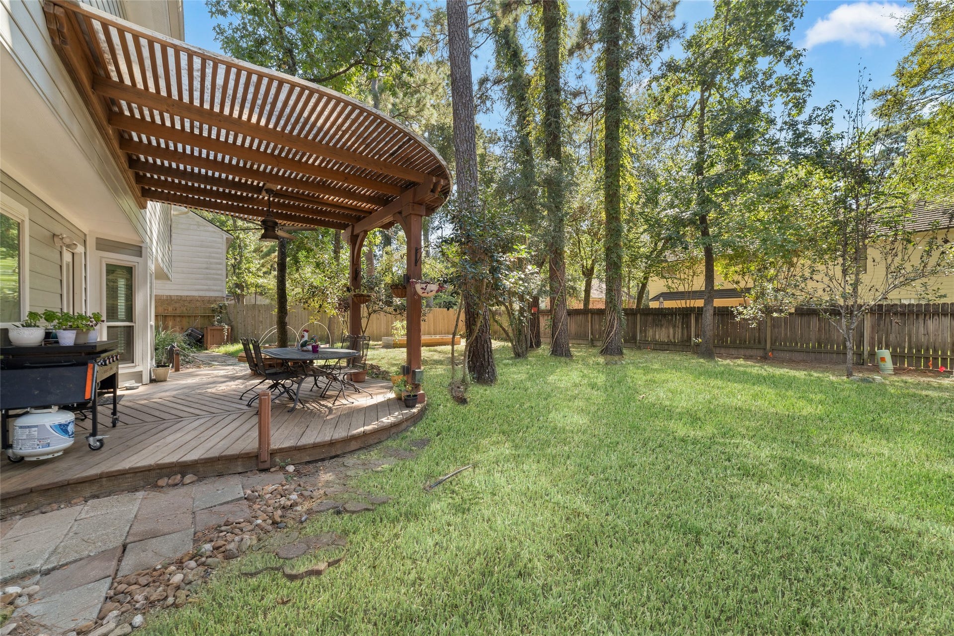 218 E Rainbow Ridge Circle, The Woodlands, TX 77381 Charming backyard retreat featuring a spacious deck with a pergola, perfect for outdoor dining and relaxation, surrounded by lush greenery and mature trees.