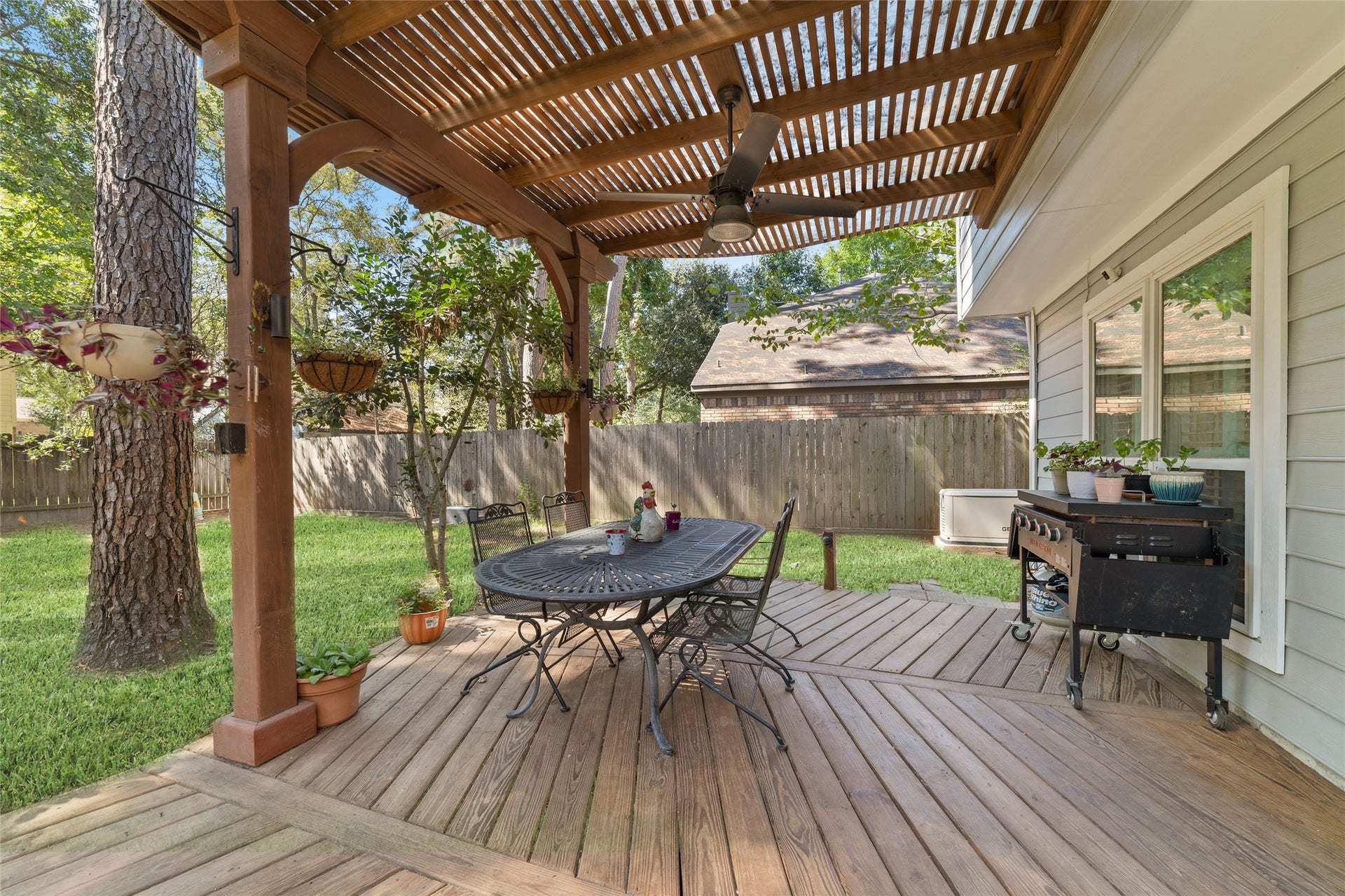 218 E Rainbow Ridge Circle, The Woodlands, TX 77381 Charming backyard retreat featuring a pergola-covered deck with a ceiling fan, perfect for outdoor dining and relaxation amidst lush greenery.