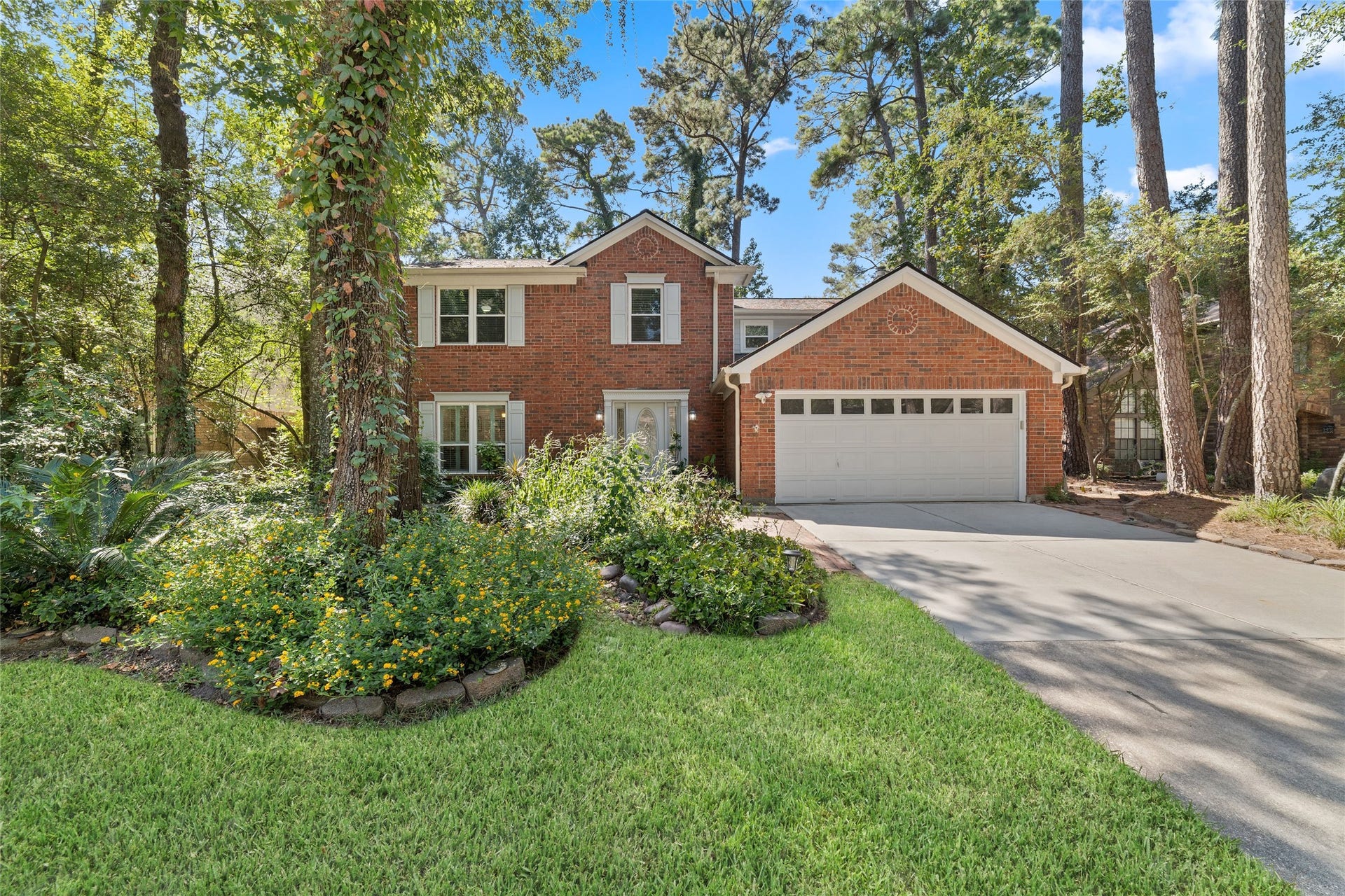 218 E Rainbow Ridge Circle, The Woodlands, TX 77381 Charming brick home nestled among mature trees, featuring a two-car garage and lush landscaped front yard.