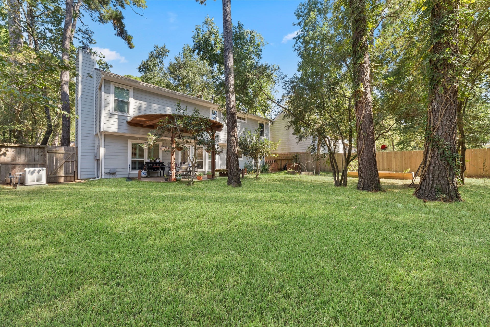 218 E Rainbow Ridge Circle, The Woodlands, TX 77381 Expansive backyard with lush greenery, mature trees, and a charming two-story home featuring a covered patio perfect for outdoor gatherings.