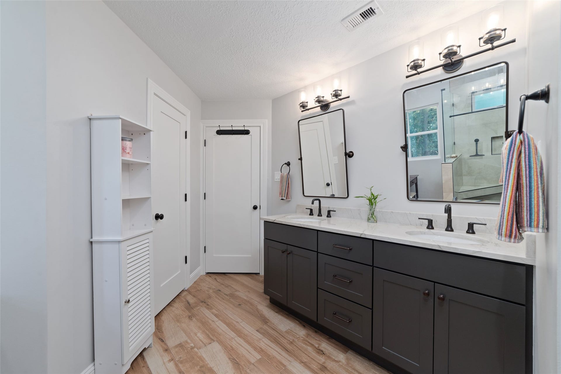 218 E Rainbow Ridge Circle, The Woodlands, TX 77381 Newly remodeled primary bathroom features a double vanity with sleek fixtures, ample storage, and elegant lighting, complemented by a light wood-look tile floor and modern design.
