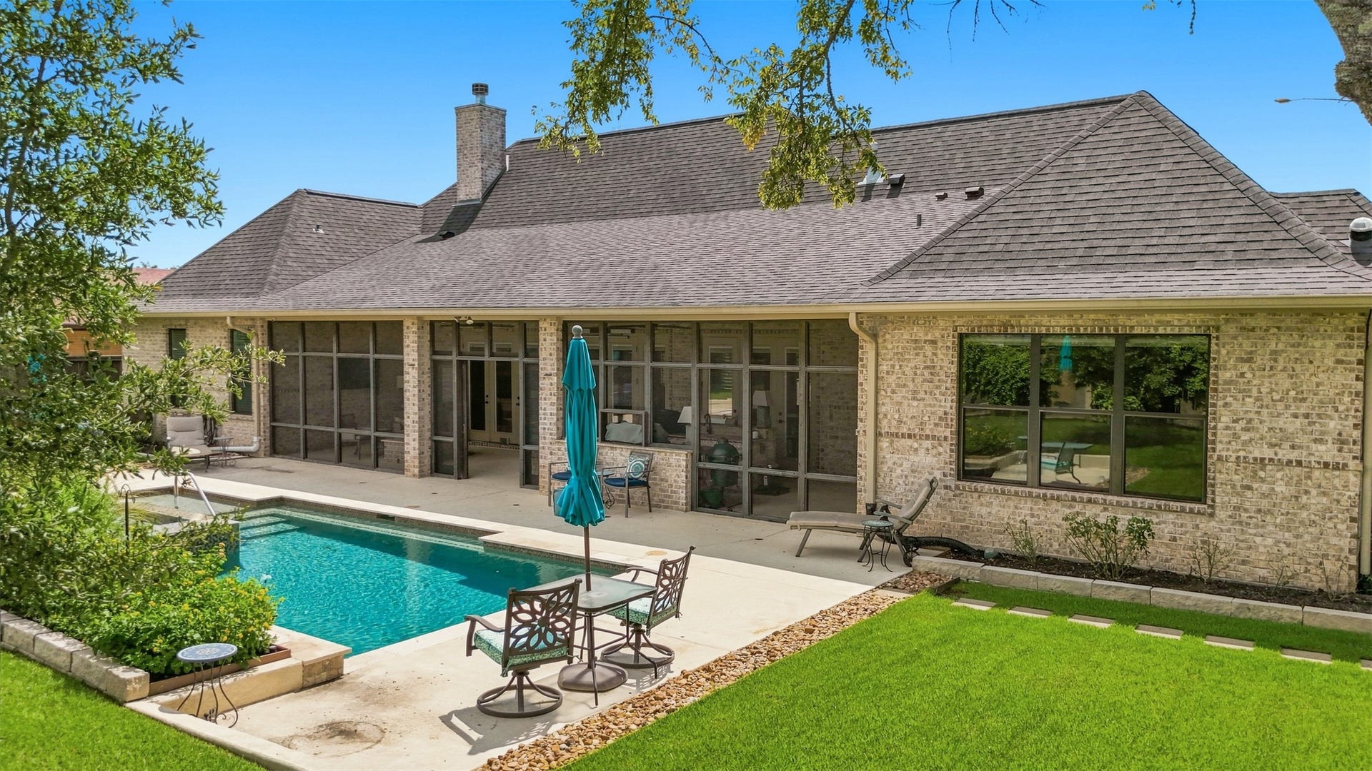 5117 Inverness Drive, Bryan, TX 77802 Backyard view showcasing the pool, manicured lawn, and screened porch spanning much of the rear of the home.