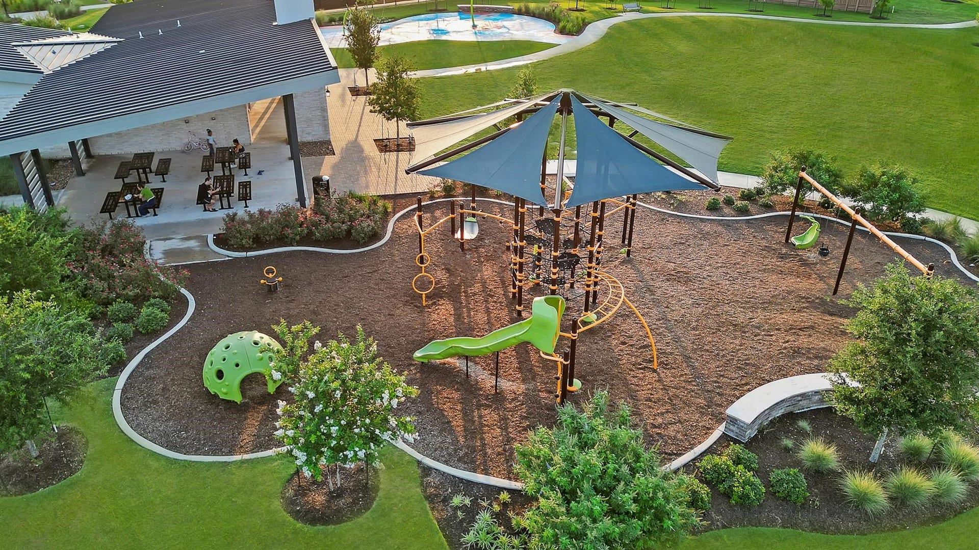 3831 Turnpike Drive, Fulshear, TX 77441 Charming outdoor space featuring a modern playground with slides and swings, surrounded by lush landscaping and adjacent to a covered seating area perfect for relaxation and gatherings.