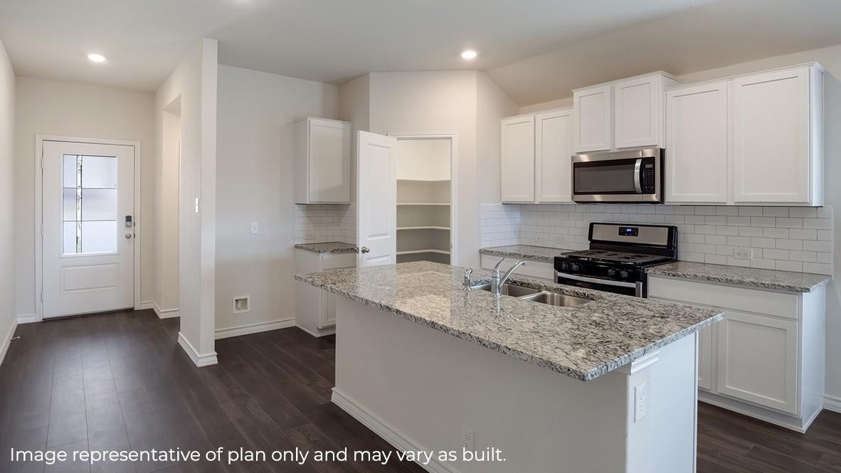 3831 Turnpike Drive, Fulshear, TX 77441 Modern kitchen with sleek granite countertops, stainless steel appliances, and ample white cabinetry. Open layout with dark hardwood floors and a convenient pantry.