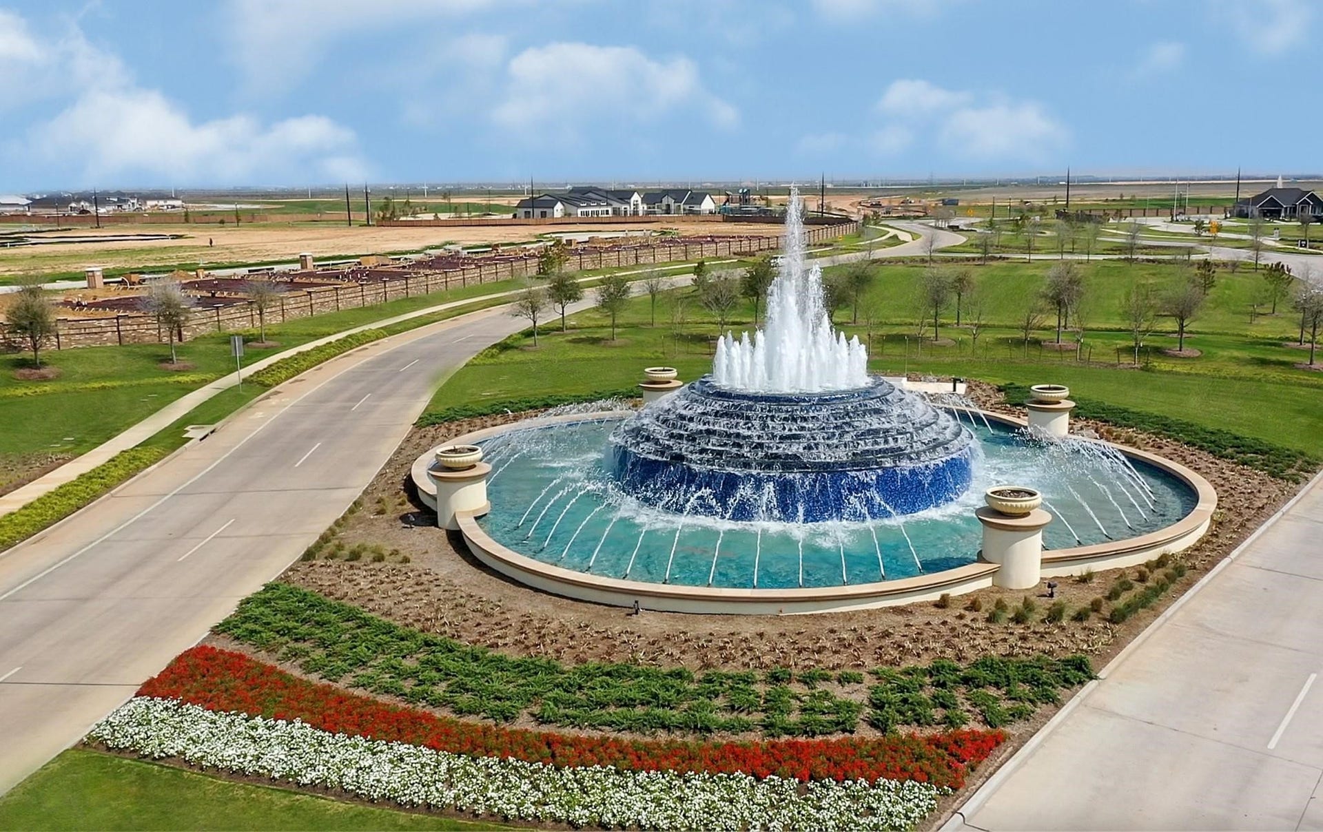 3831 Turnpike Drive, Fulshear, TX 77441 Stunning landscaped roundabout featuring a grand, multi-tiered fountain surrounded by vibrant flowerbeds and lush greenery, offering a welcoming entrance to the community.