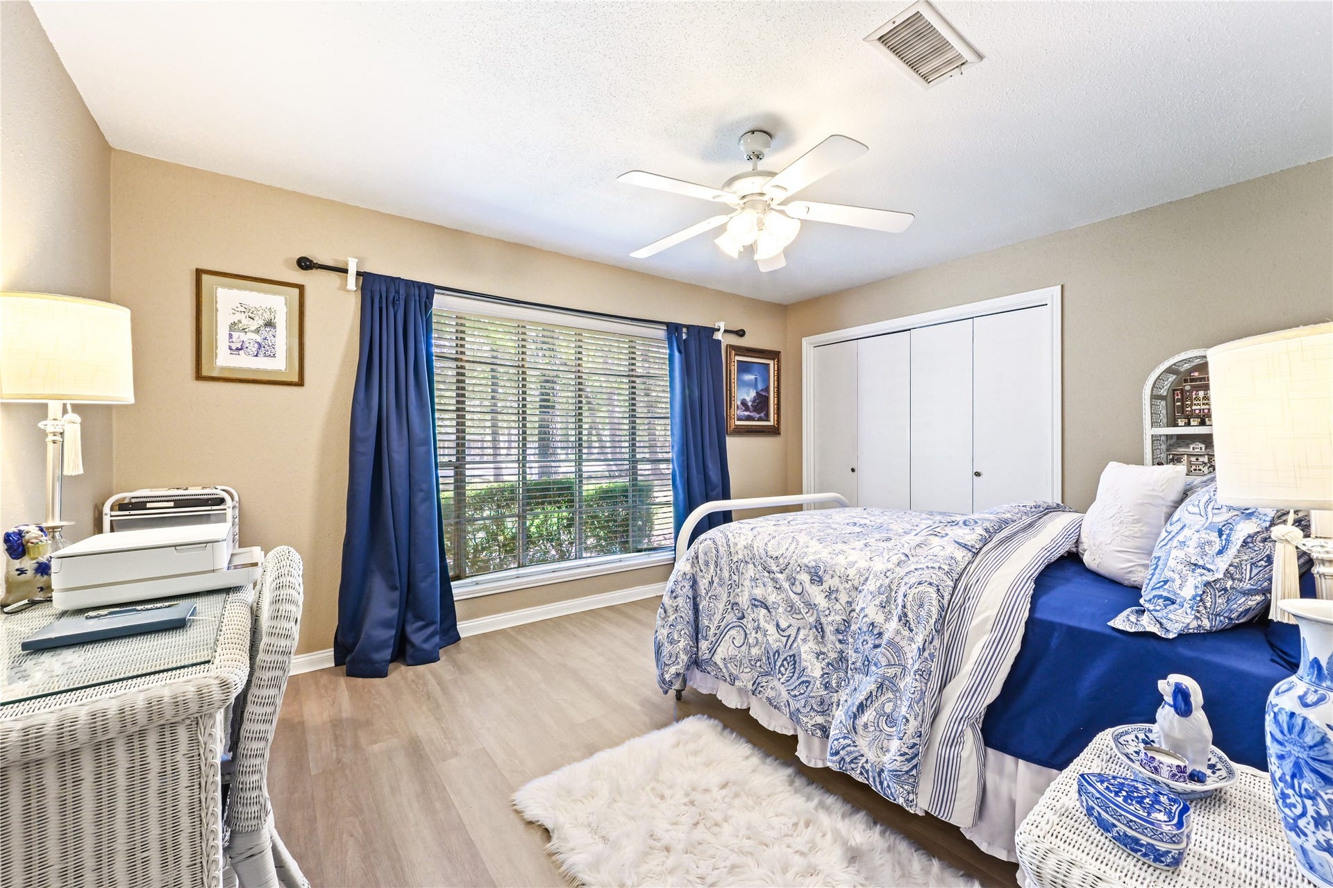25803 Maplewood Drive, Spring, TX 77386 Charming bedroom with natural light through large windows, elegant blue accents, and a cozy atmosphere enhanced by a ceiling fan and soft lighting.