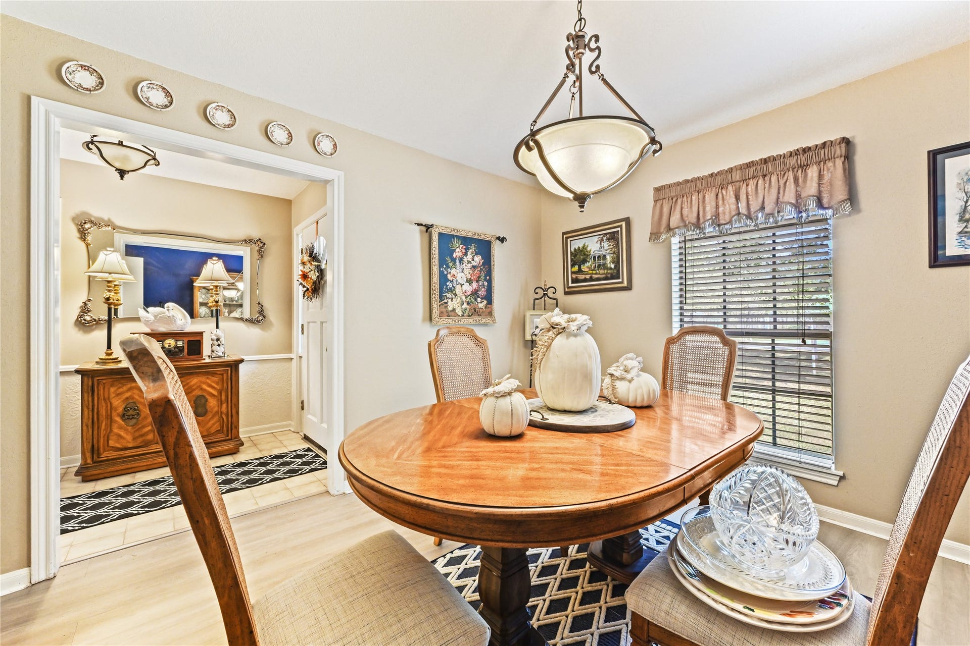 25803 Maplewood Drive, Spring, TX 77386 Elegant dining area with abundant natural light, featuring a classic wooden table and tasteful decor, seamlessly connected to a charming hallway with decorative wall plates and sophisticated lighting.