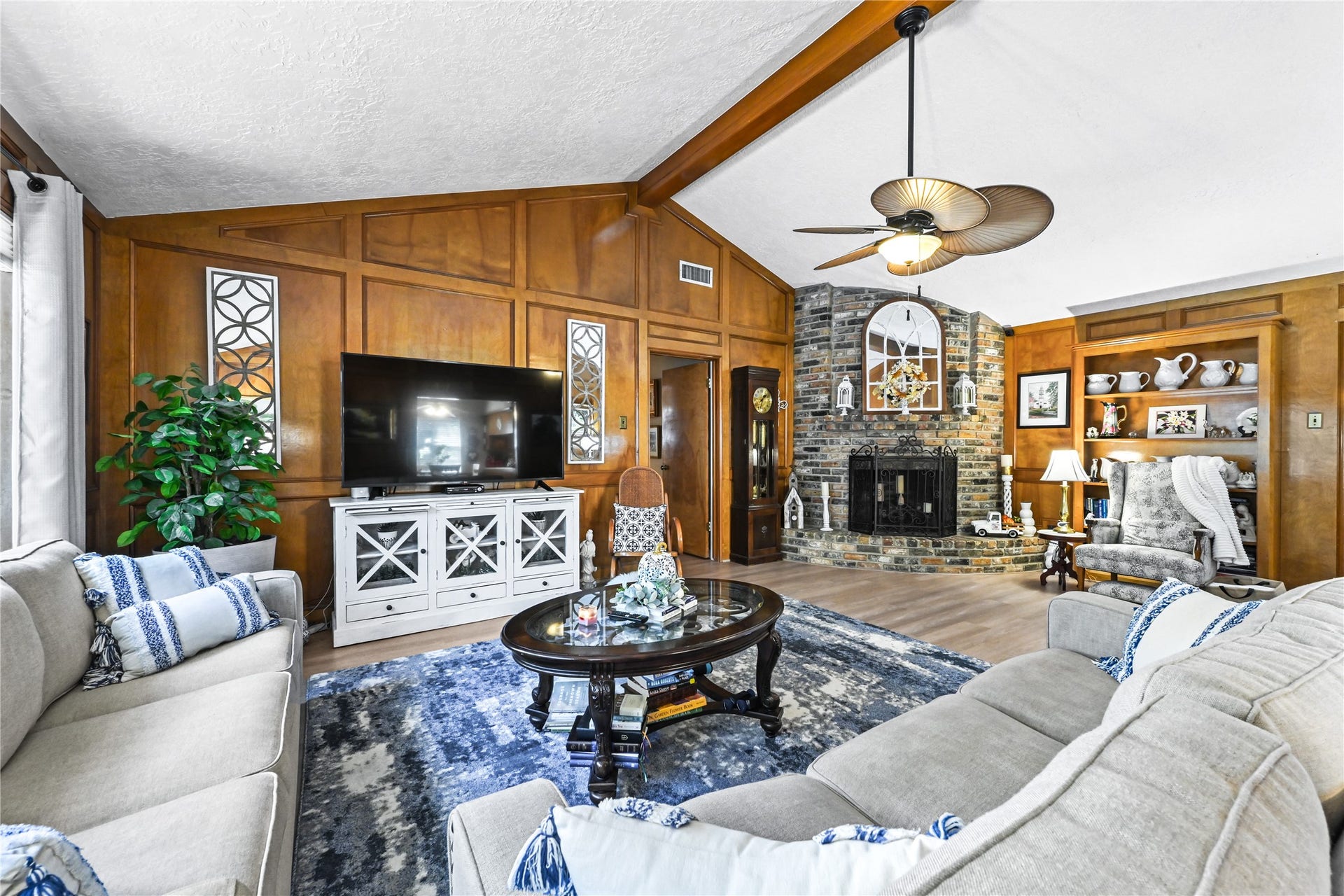 25803 Maplewood Drive, Spring, TX 77386 Charming living room featuring a cozy stone fireplace, rich wood paneling, and a vaulted ceiling with an elegant fan. The space is complemented by plush sofas, built-in shelving, and abundant natural light.