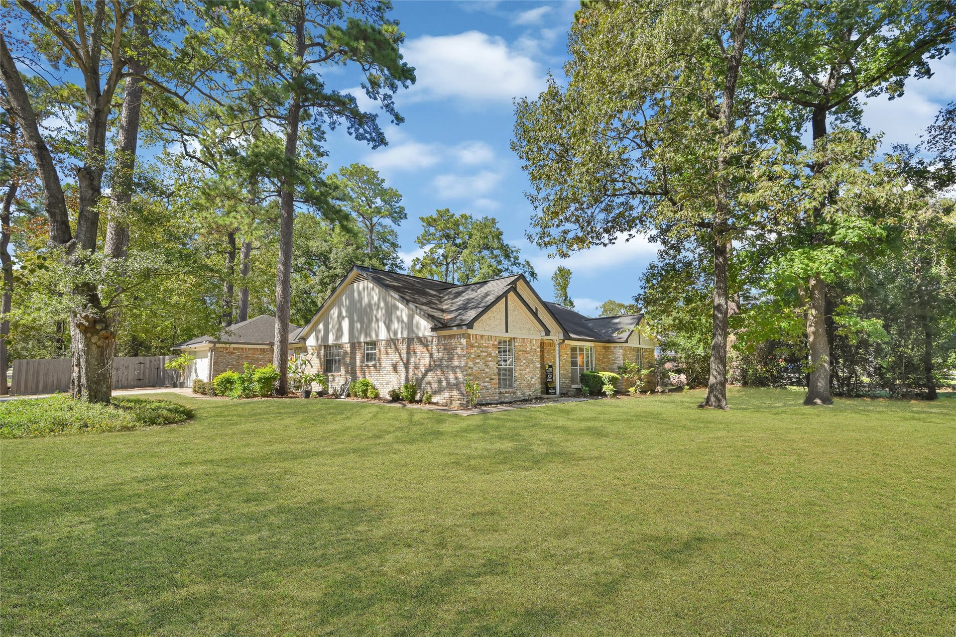 25803 Maplewood Drive, Spring, TX 77386 Charming brick home nestled among mature trees, offering a spacious and lush green lawn ideal for outdoor enjoyment.