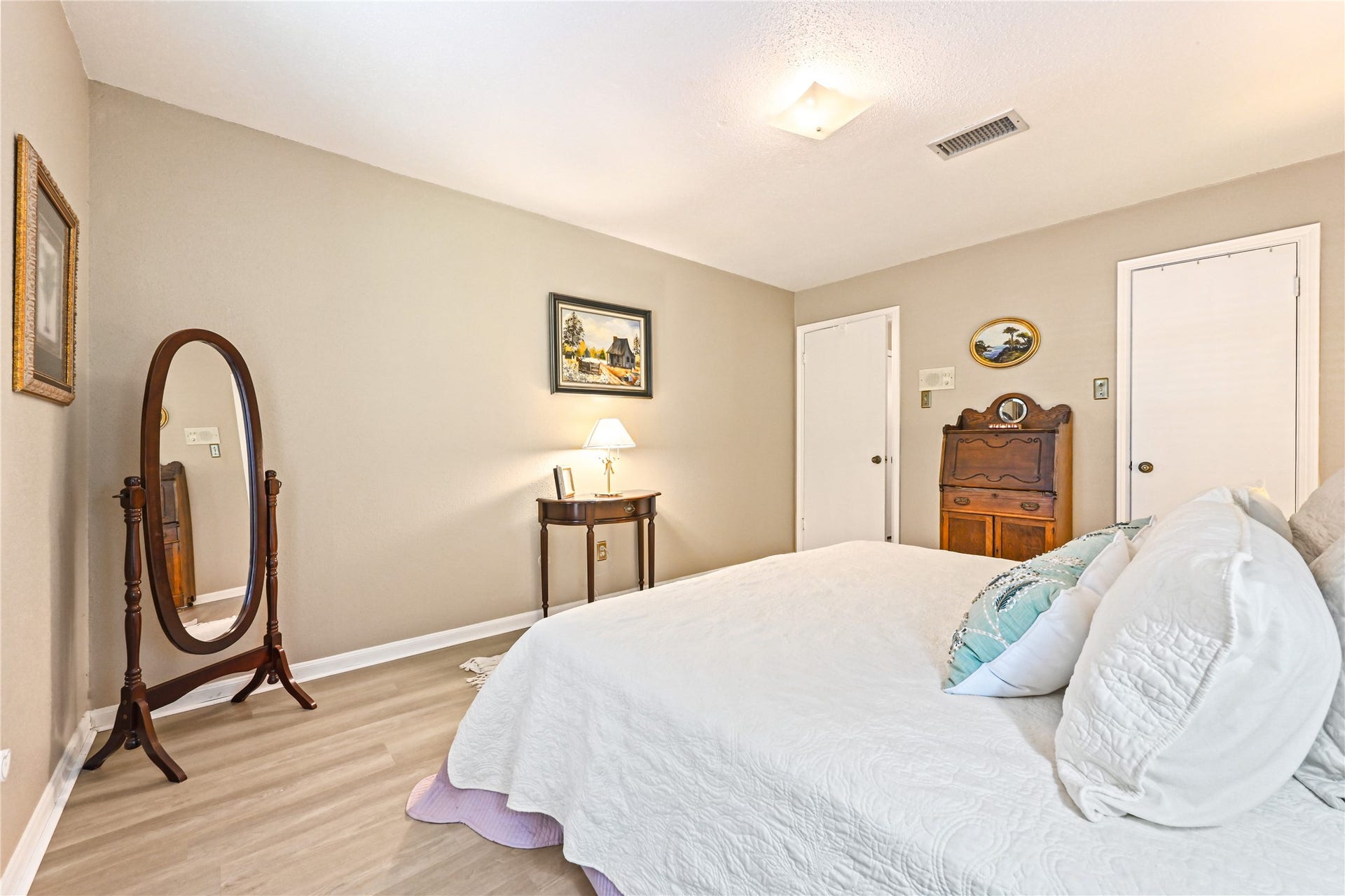 25803 Maplewood Drive, Spring, TX 77386 Cozy bedroom with soft neutral walls, featuring a comfortable bed adorned with decorative pillows. A classic floor mirror and elegant wooden furniture add charm, while ample natural light enhances the inviting atmosphere.