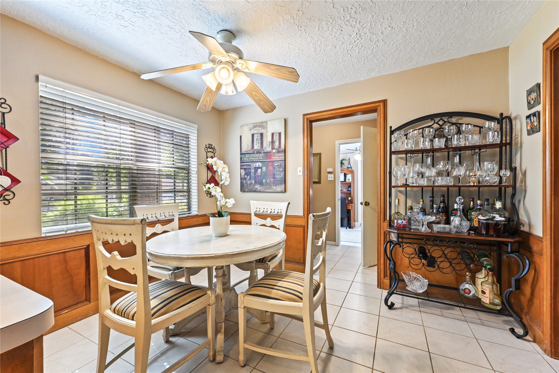 25803 Maplewood Drive, Spring, TX 77386 Cozy dining area with a round table and chairs, highlighted by natural light streaming through large windows. A ceiling fan and stylish bar cart add charm and functionality.