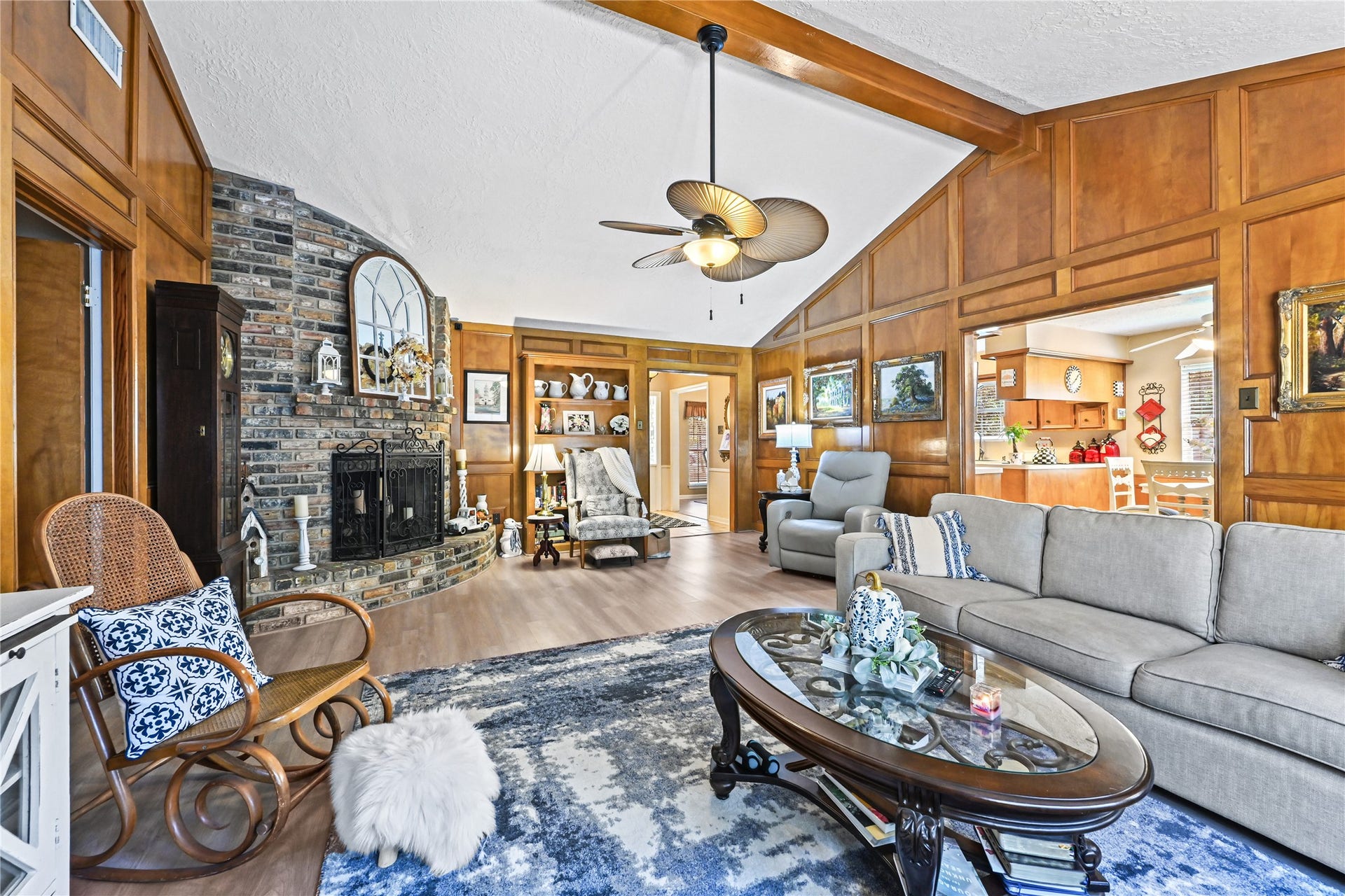 25803 Maplewood Drive, Spring, TX 77386 Charming living room featuring vaulted ceilings and warm wood paneling, highlighted by a cozy brick fireplace. The open layout seamlessly connects to a bright kitchen, perfect for entertaining.