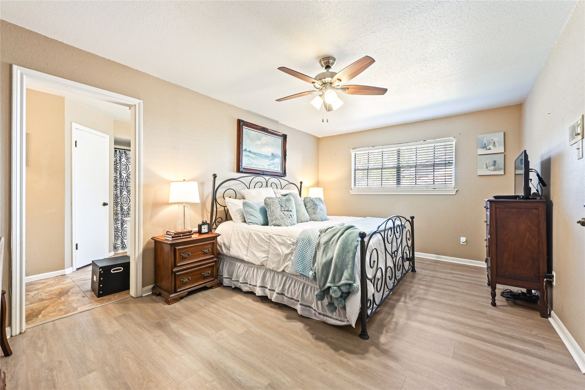 25803 Maplewood Drive, Spring, TX 77386 Cozy bedroom featuring a stylish wrought iron bed, warm laminate flooring, and ample natural light from a large window, complemented by a ceiling fan for added comfort.
