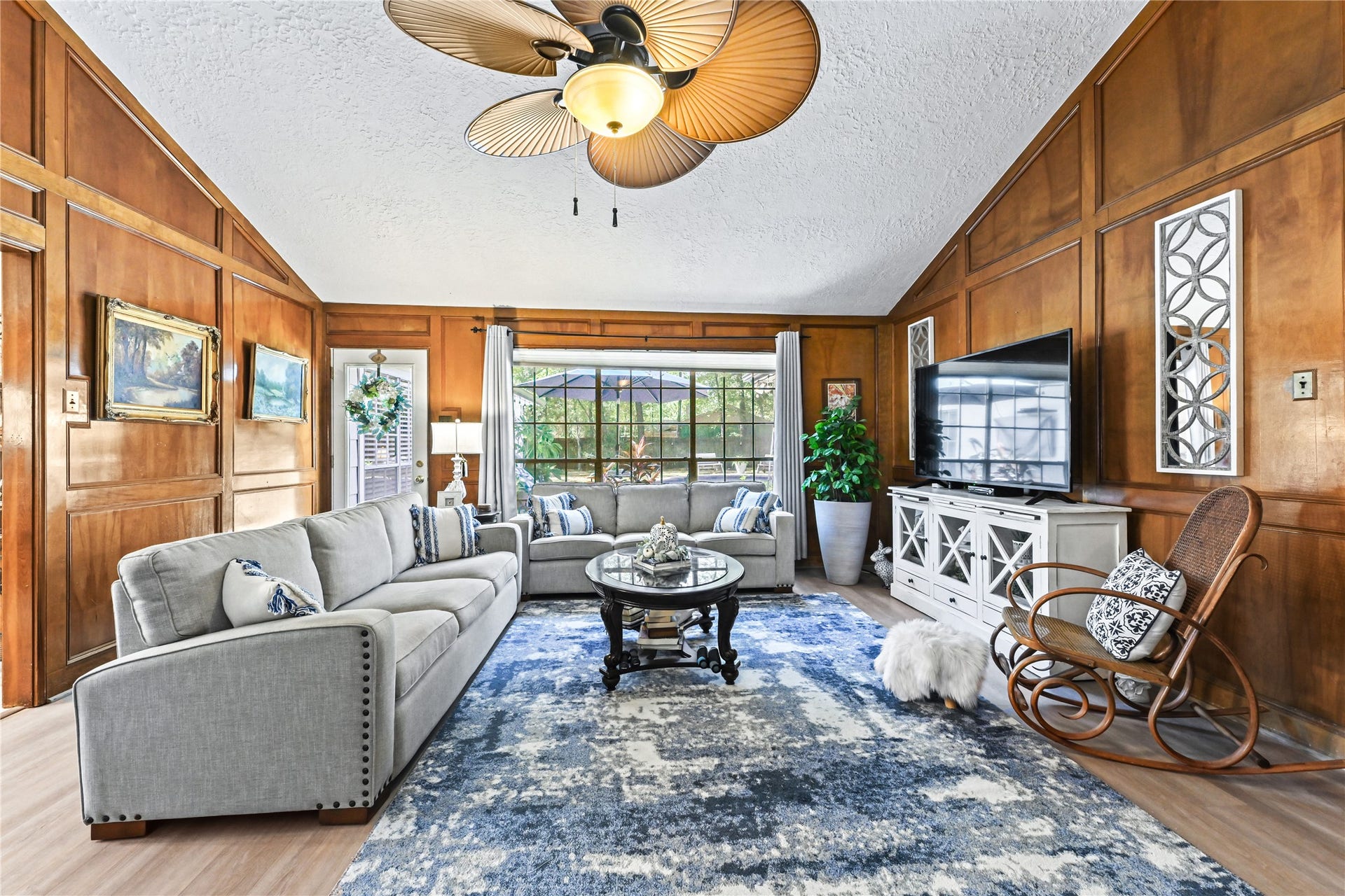 25803 Maplewood Drive, Spring, TX 77386 Elegant living room with rich wood paneling, plenty of natural light, and stylish furnishings including a cozy gray sofa and modern accents.