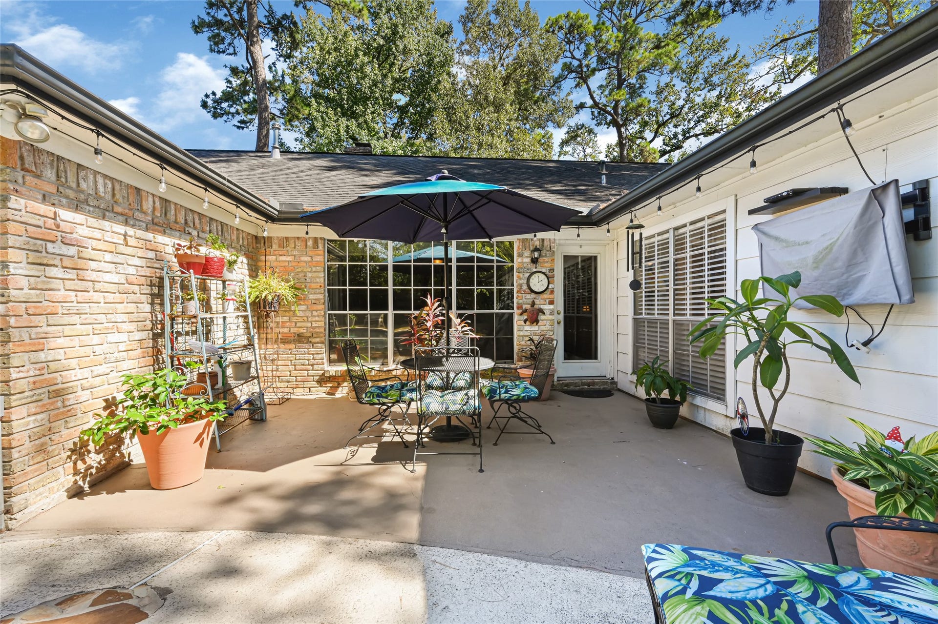 25803 Maplewood Drive, Spring, TX 77386 Charming outdoor patio with lush potted plants, cozy seating, and a large umbrella, perfect for relaxing or entertaining under the open sky.