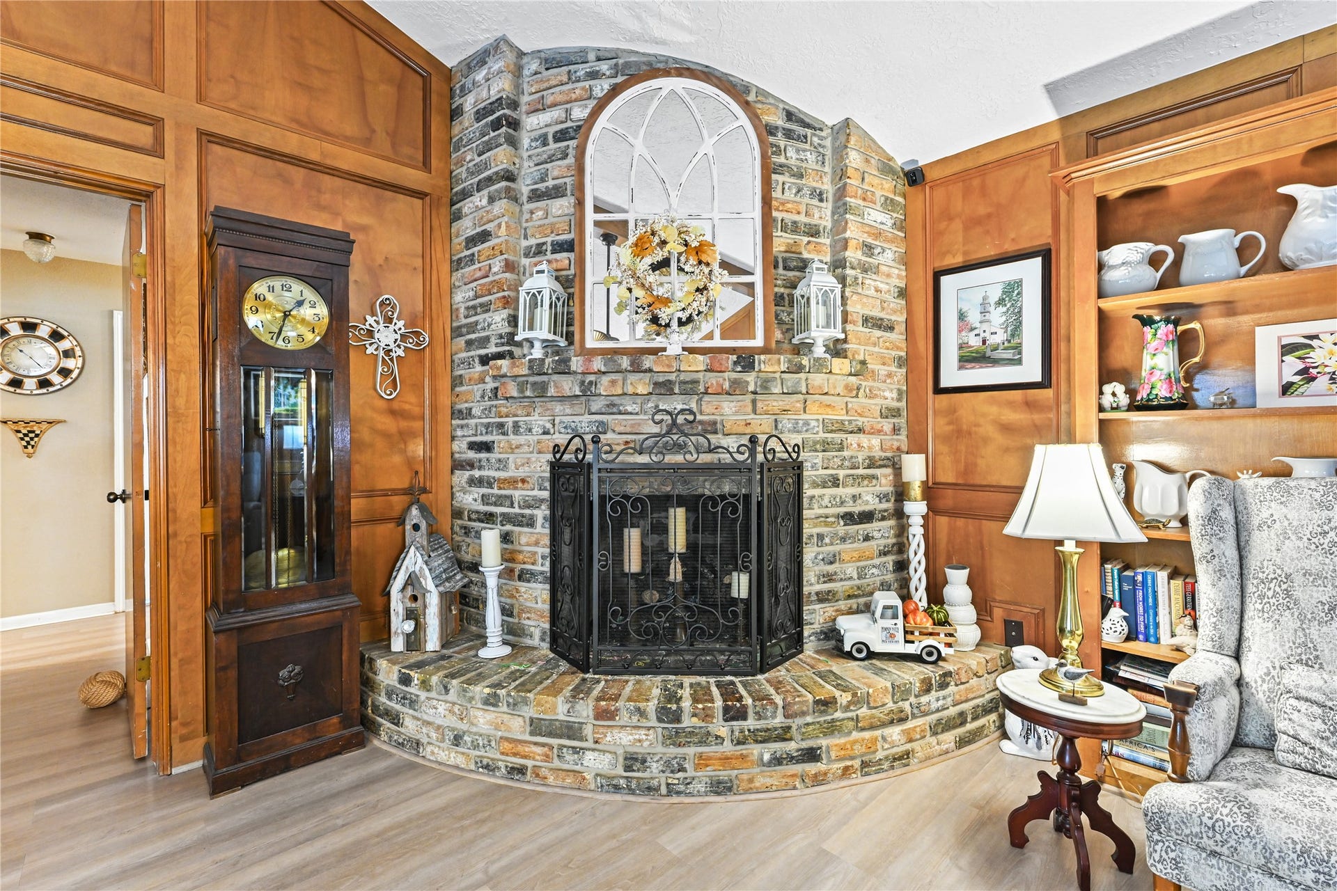 25803 Maplewood Drive, Spring, TX 77386 Charming living area featuring a rustic brick fireplace surrounded by rich wood paneling, a classic grandfather clock, and elegant built-in shelving.