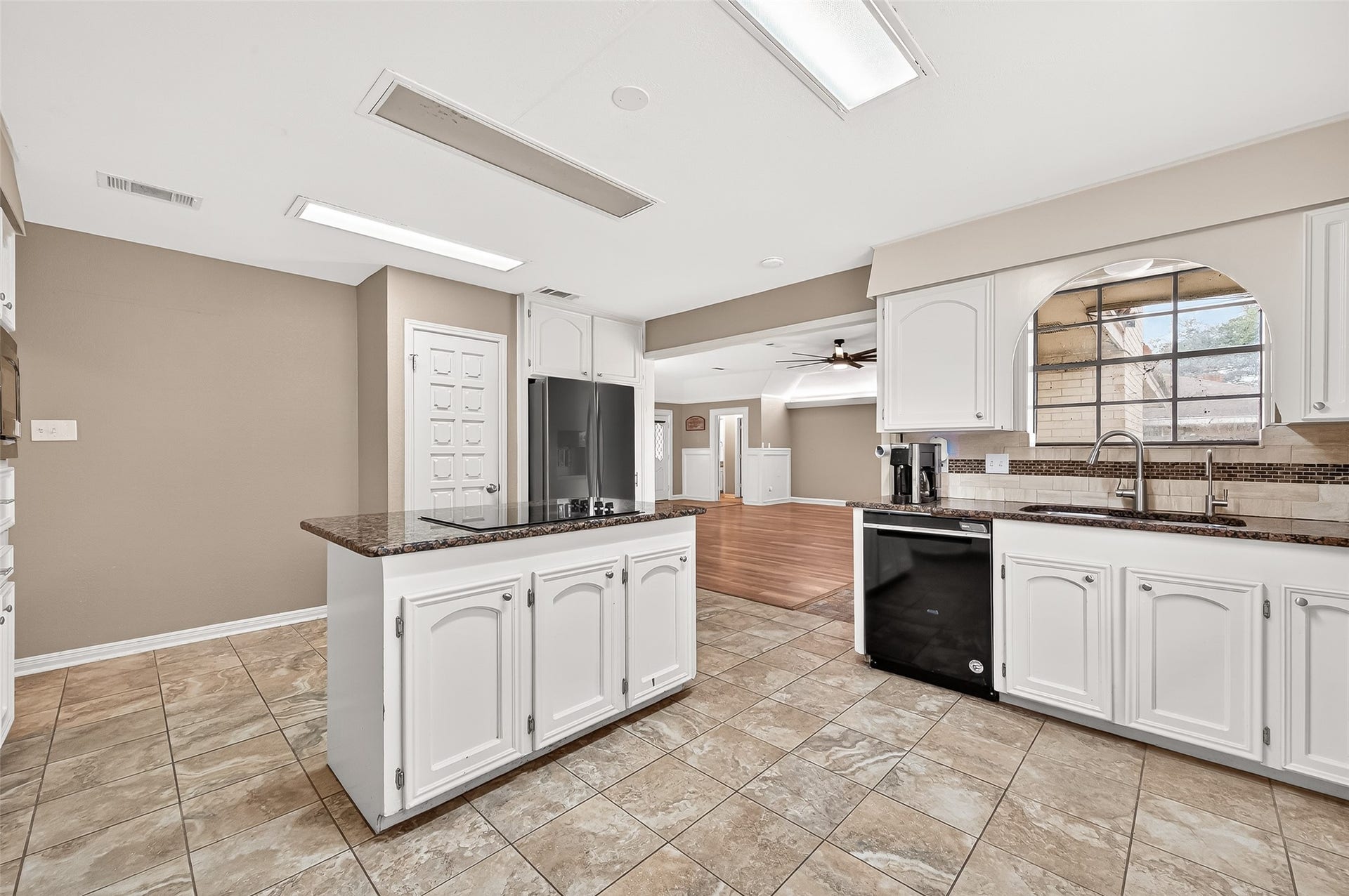 5607 Avenue M 1/2, Santa Fe, TX 77510 This photo showcases a modern kitchen with white cabinetry, granite countertops, and tile flooring. It features stainless steel appliances and an open layout leading to a living area with wood flooring and a ceiling fan. The space is bright and welcoming, ideal for entertaining.