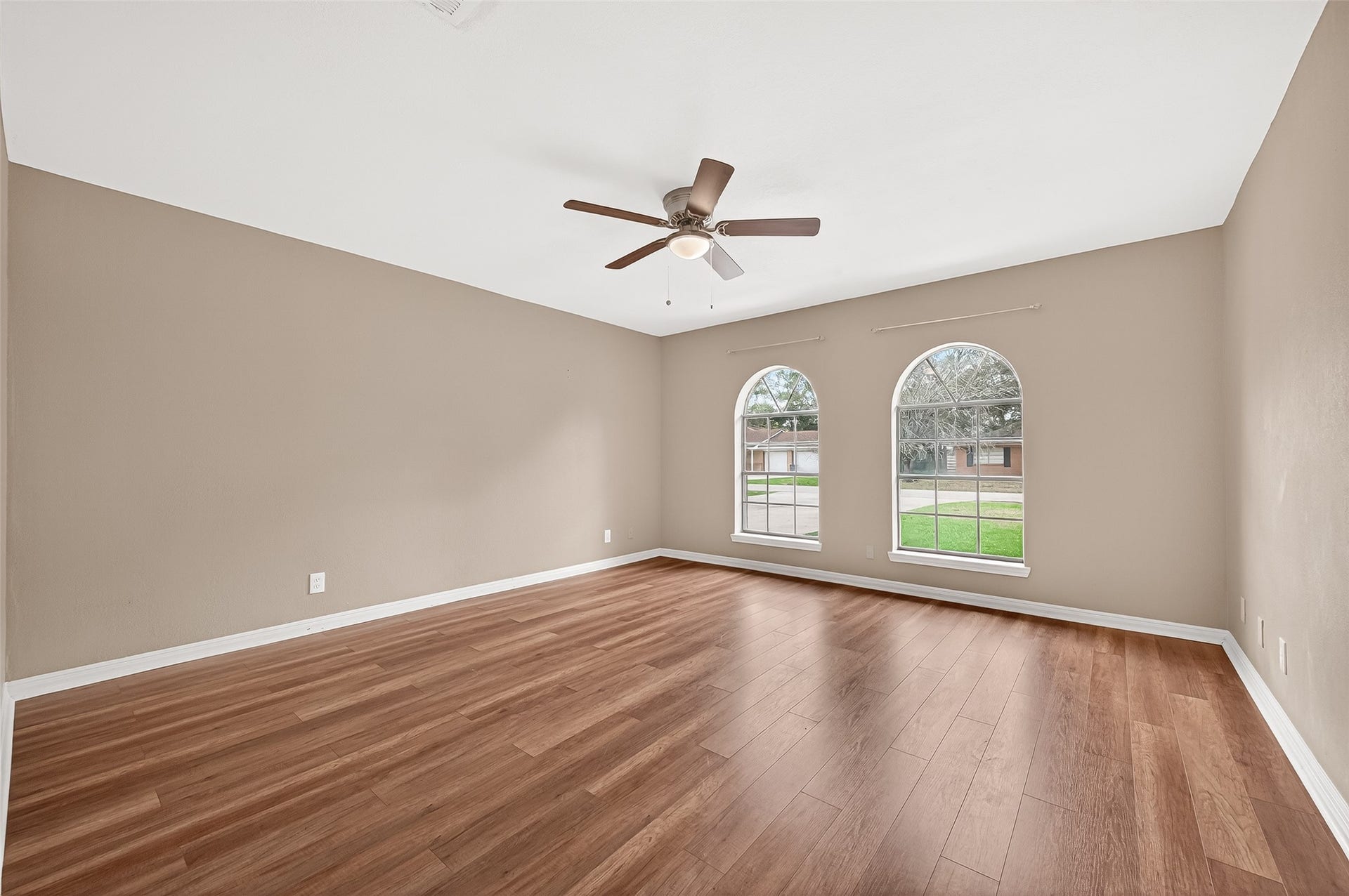 5607 Avenue M 1/2, Santa Fe, TX 77510 Primary bedroom with warm wood flooring, neutral walls, and a ceiling fan. Features two large arched windows providing plenty of natural light and a view of the front yard. Perfect for a cozy living area or bedroom.