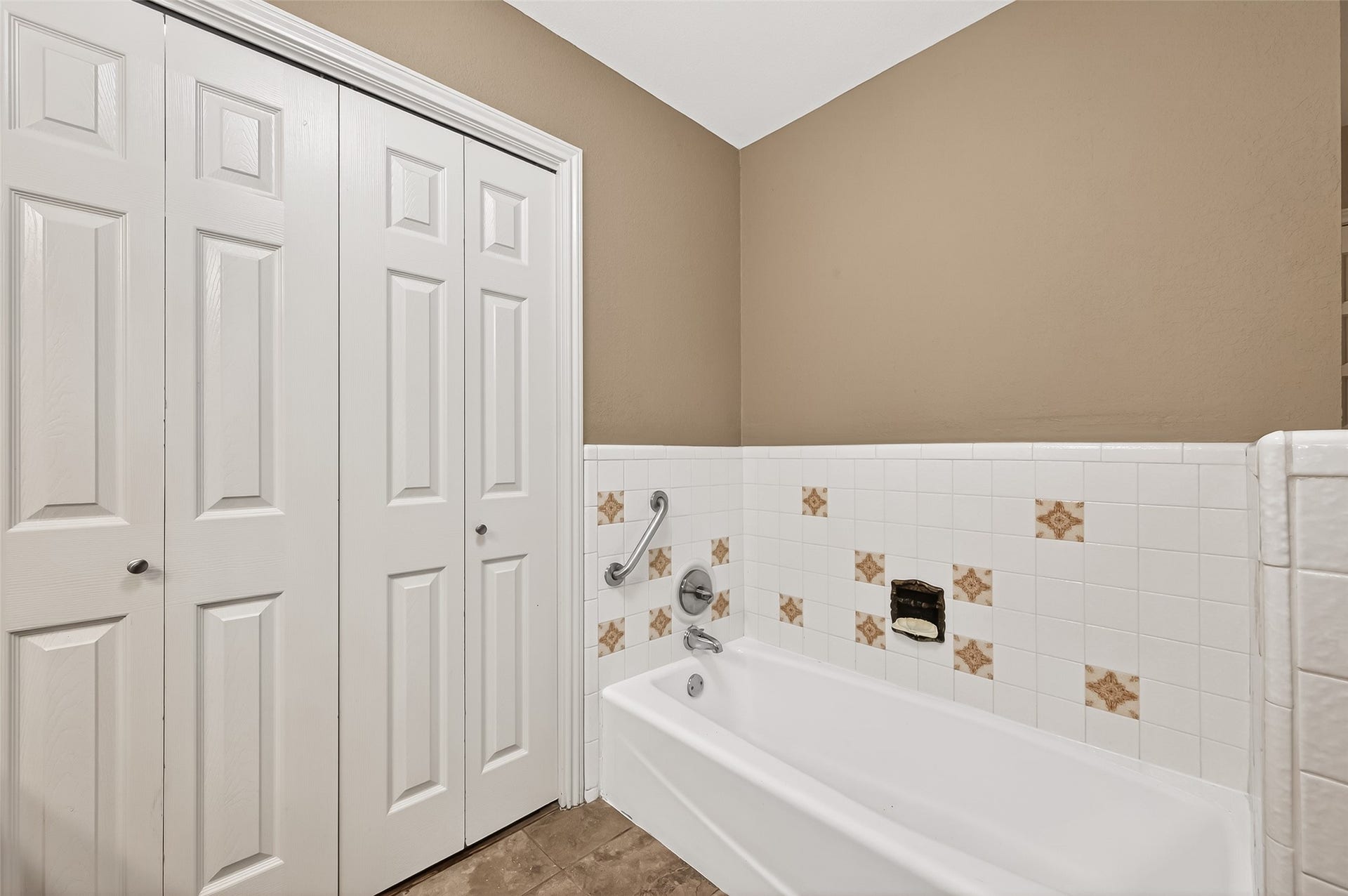 5607 Avenue M 1/2, Santa Fe, TX 77510 This bathroom features a bathtub with vintage tile accents, a grab bar for safety, and a closet with white paneled doors, offering both style and functionality.