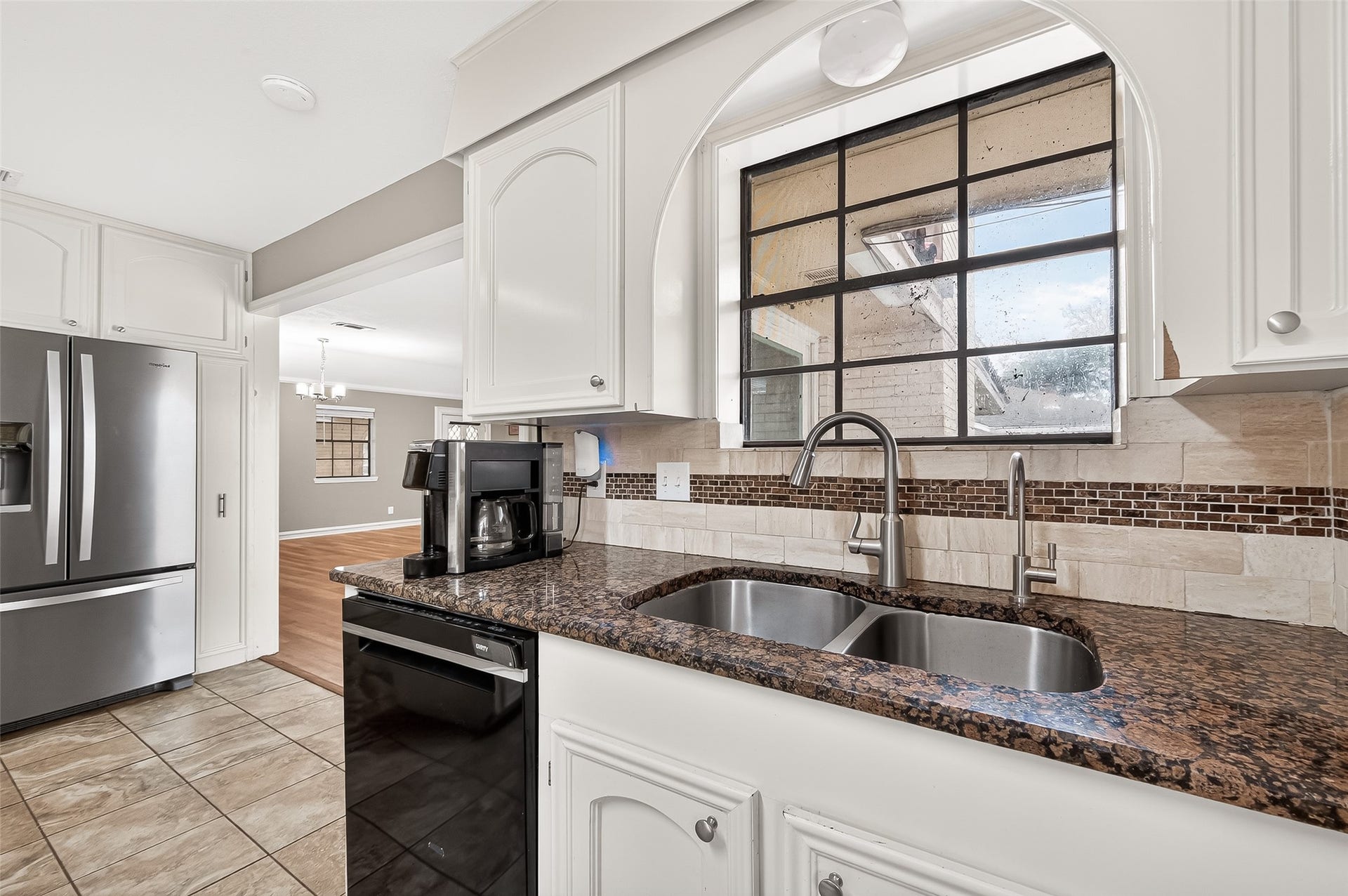 5607 Avenue M 1/2, Santa Fe, TX 77510 Modern kitchen with granite countertops, dual sinks, and stainless steel appliances. Features a large window for natural light, white cabinetry, and a view into the adjacent dining area. Large kitchen window overlooking the backyard.