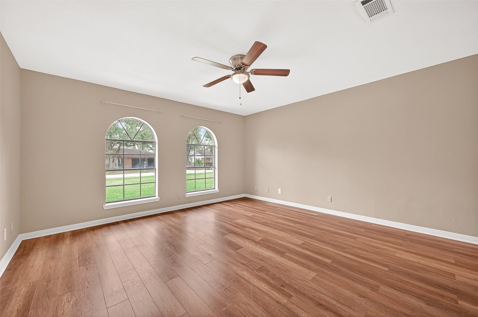 5607 Avenue M 1/2, Santa Fe, TX 77510 This spacious room features elegant wood flooring, two large arched windows providing ample natural light, neutral walls, and a ceiling fan for comfort.