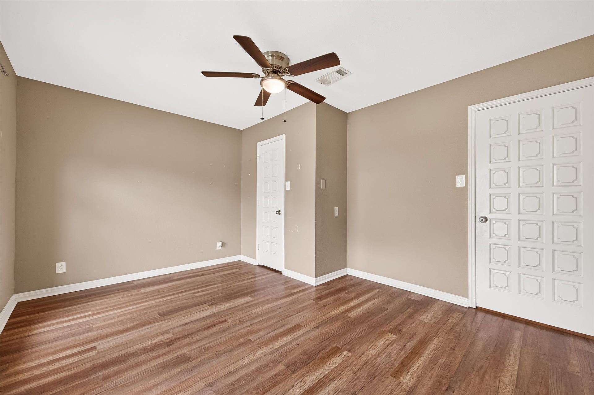5607 Avenue M 1/2, Santa Fe, TX 77510 This room features warm beige walls, hardwood floors, and a ceiling fan. It's bright and inviting, with two doors for easy access. Ideal for a bedroom or home office.
