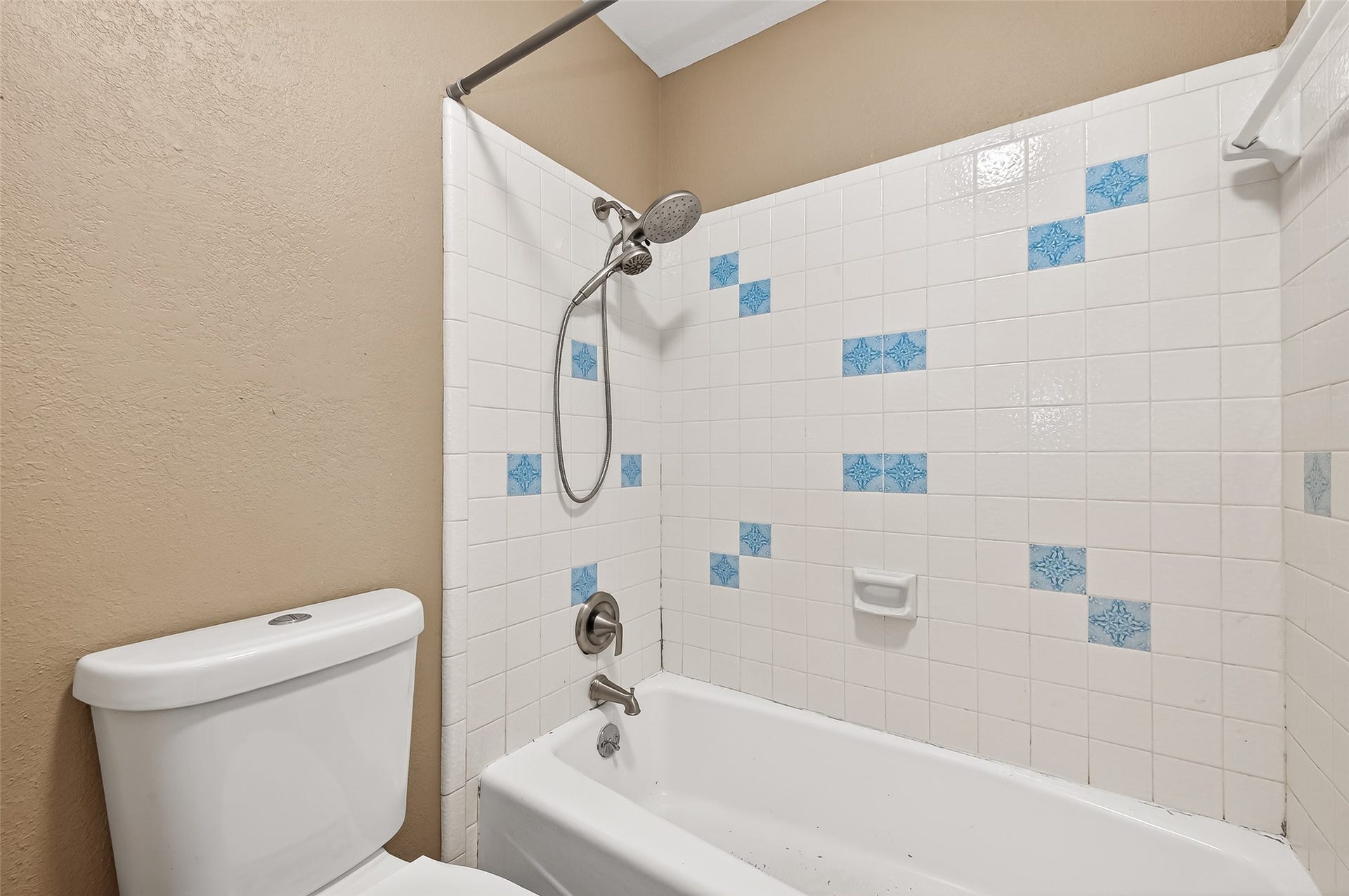5607 Avenue M 1/2, Santa Fe, TX 77510 Cozy bathroom featuring a bathtub with a showerhead, accented by white tiles with blue patterns. Neutral wall color complements the clean, functional design.