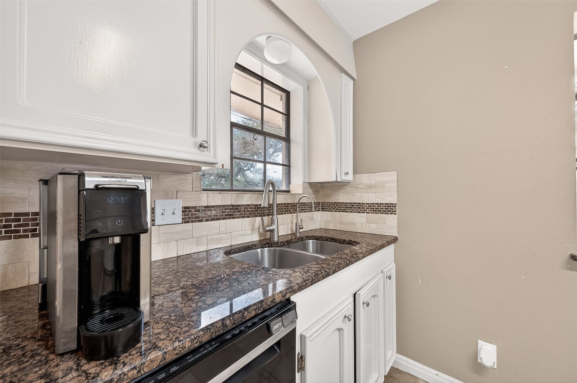 5607 Avenue M 1/2, Santa Fe, TX 77510 This kitchen features a sleek design with granite countertops, and a double sink. It includes white cabinetry, a tile backsplash, and a large window for natural light.