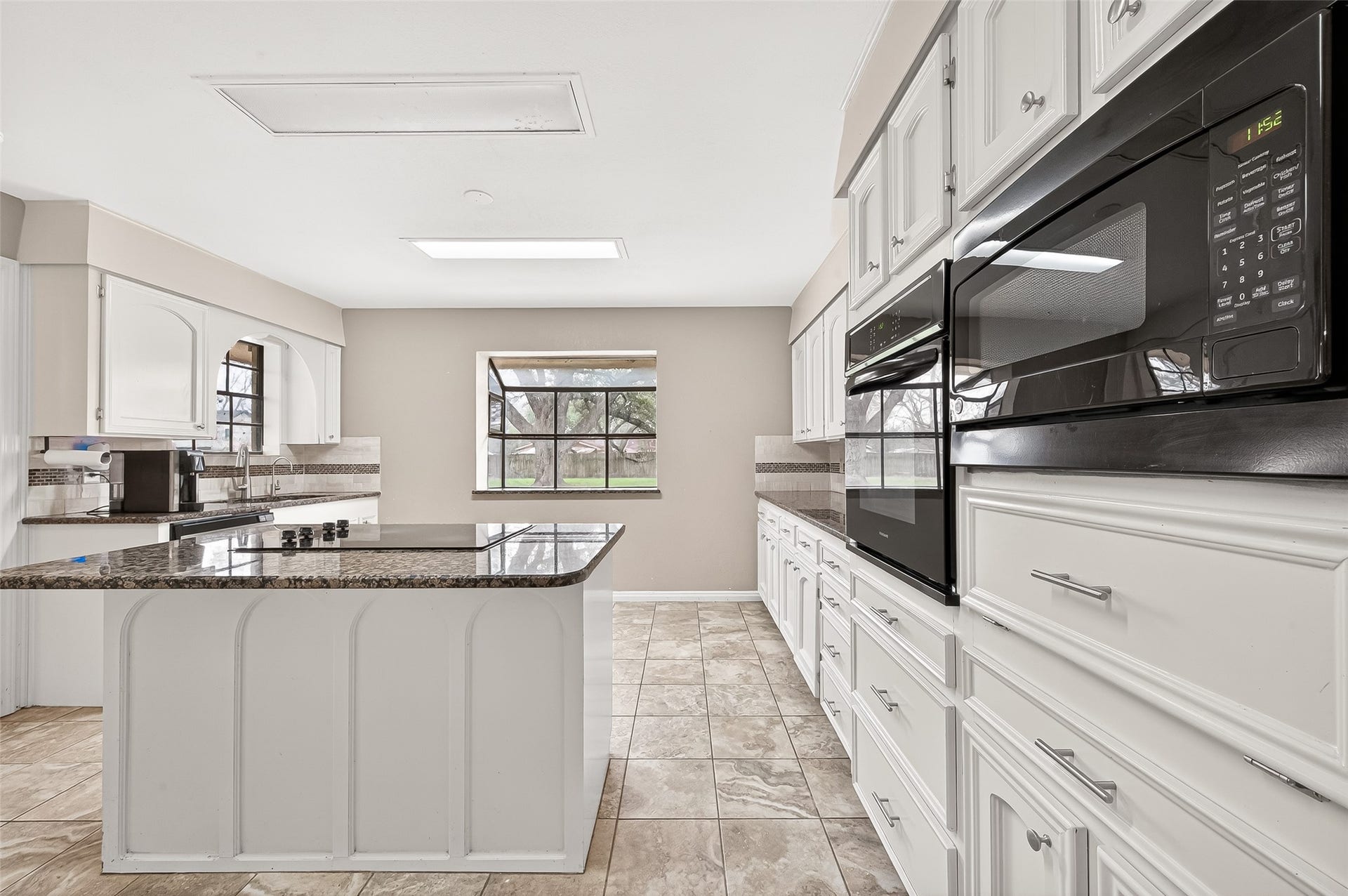5607 Avenue M 1/2, Santa Fe, TX 77510 Spacious kitchen with a large island, granite countertops, and ample white cabinetry. Features modern appliances, tiled flooring, and a window with a pleasant view.