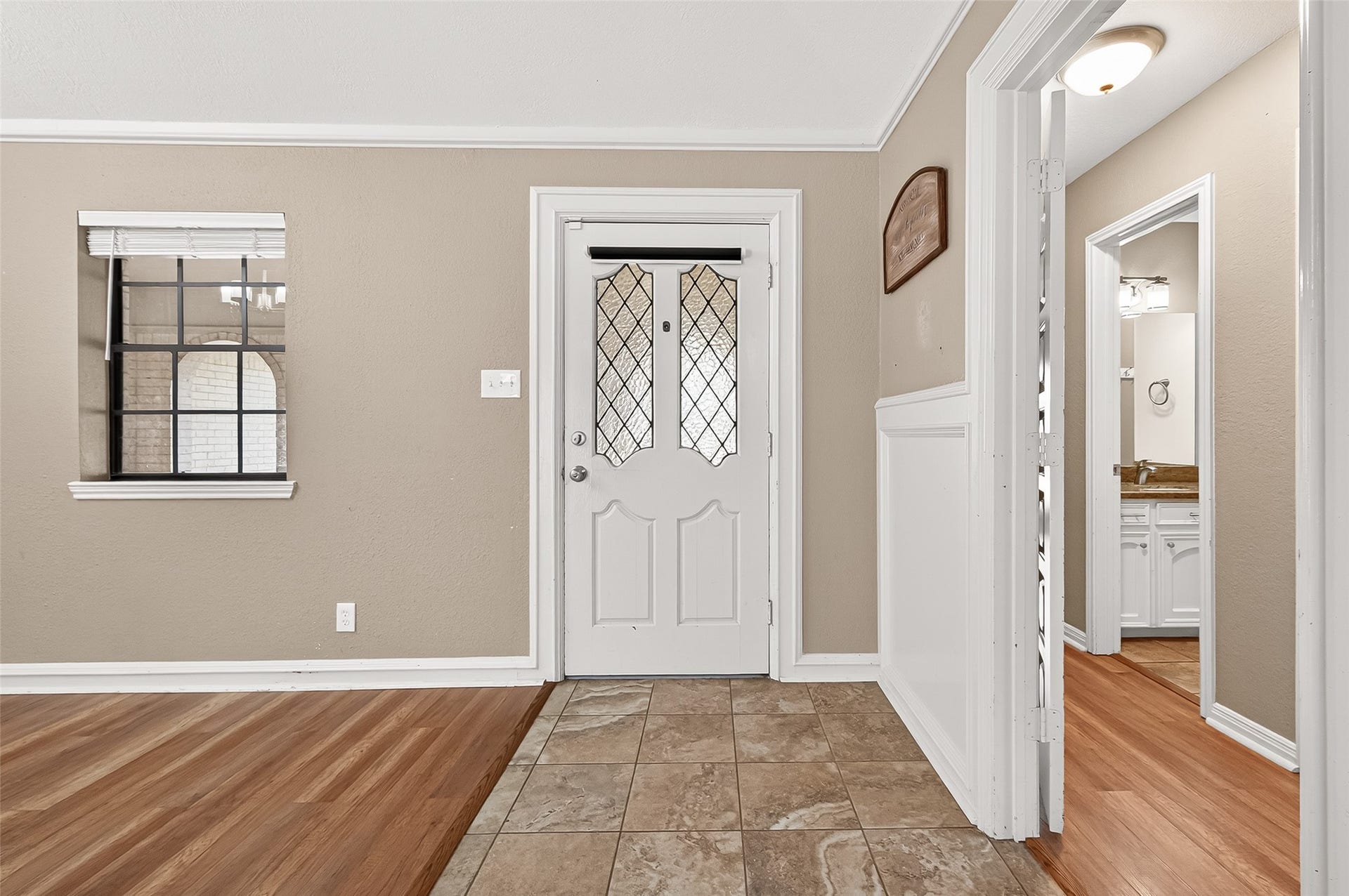 5607 Avenue M 1/2, Santa Fe, TX 77510 This photo showcases a cozy entryway with a white door featuring decorative glass panels. The space has a mix of tile and wood flooring, beige walls, and wainscoting.