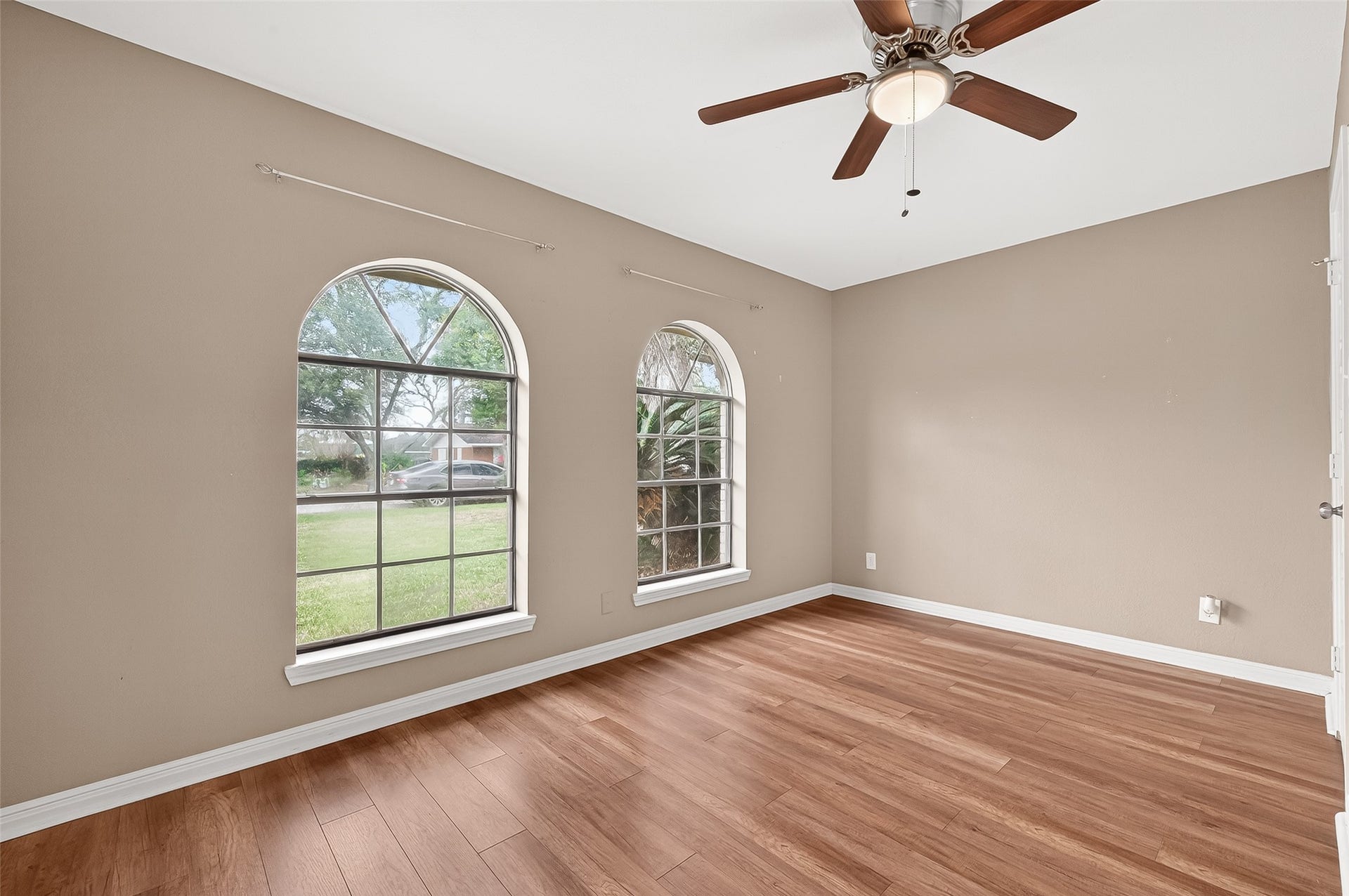 5607 Avenue M 1/2, Santa Fe, TX 77510 This room features two large arched windows, allowing natural light to fill the space. It has warm wood flooring, neutral walls, and a ceiling fan, creating a cozy and inviting atmosphere.