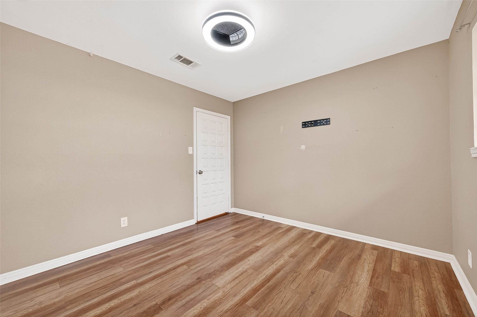 5607 Avenue M 1/2, Santa Fe, TX 77510 This photo shows a simple, unfurnished room with beige walls and wood flooring. It features a modern ceiling light and a door, creating a clean and versatile space ready for customization.
