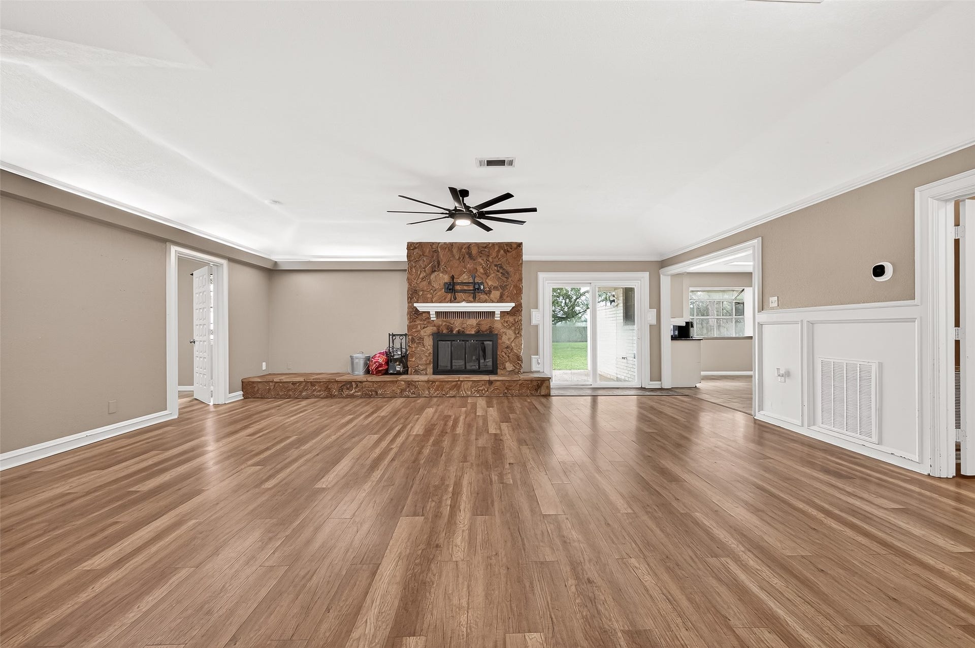 5607 Avenue M 1/2, Santa Fe, TX 77510 Spacious living room with hardwood floors, a central stone wood burning fireplace, and large windows offering natural light. A ceiling fan adds comfort, while sliding doors lead to a lush backyard, perfect for indoor-outdoor living.