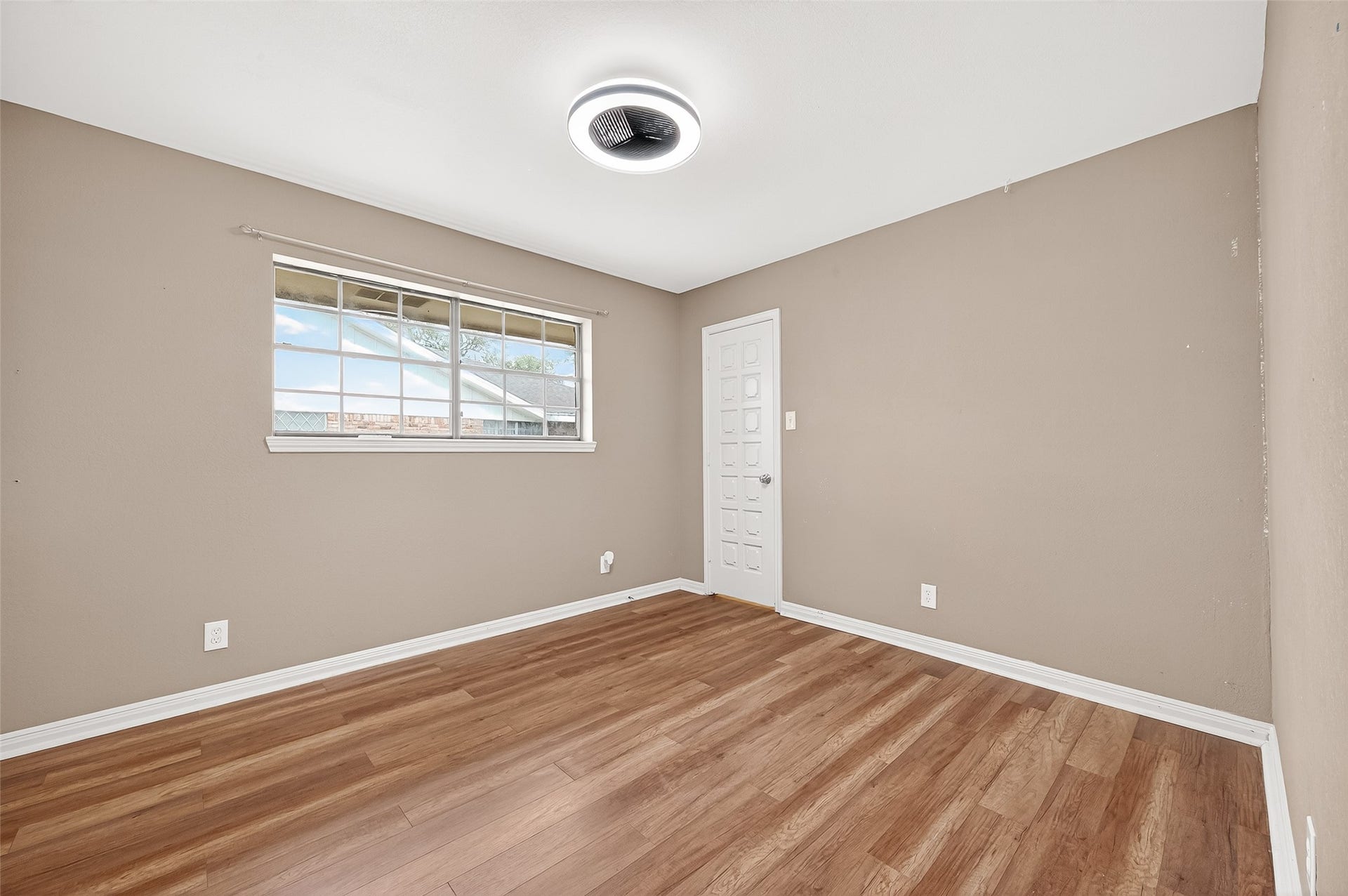 5607 Avenue M 1/2, Santa Fe, TX 77510 This room features neutral-colored walls, wood flooring, and a large window for natural light. The modern ceiling light and simple door add to its clean, fresh look.