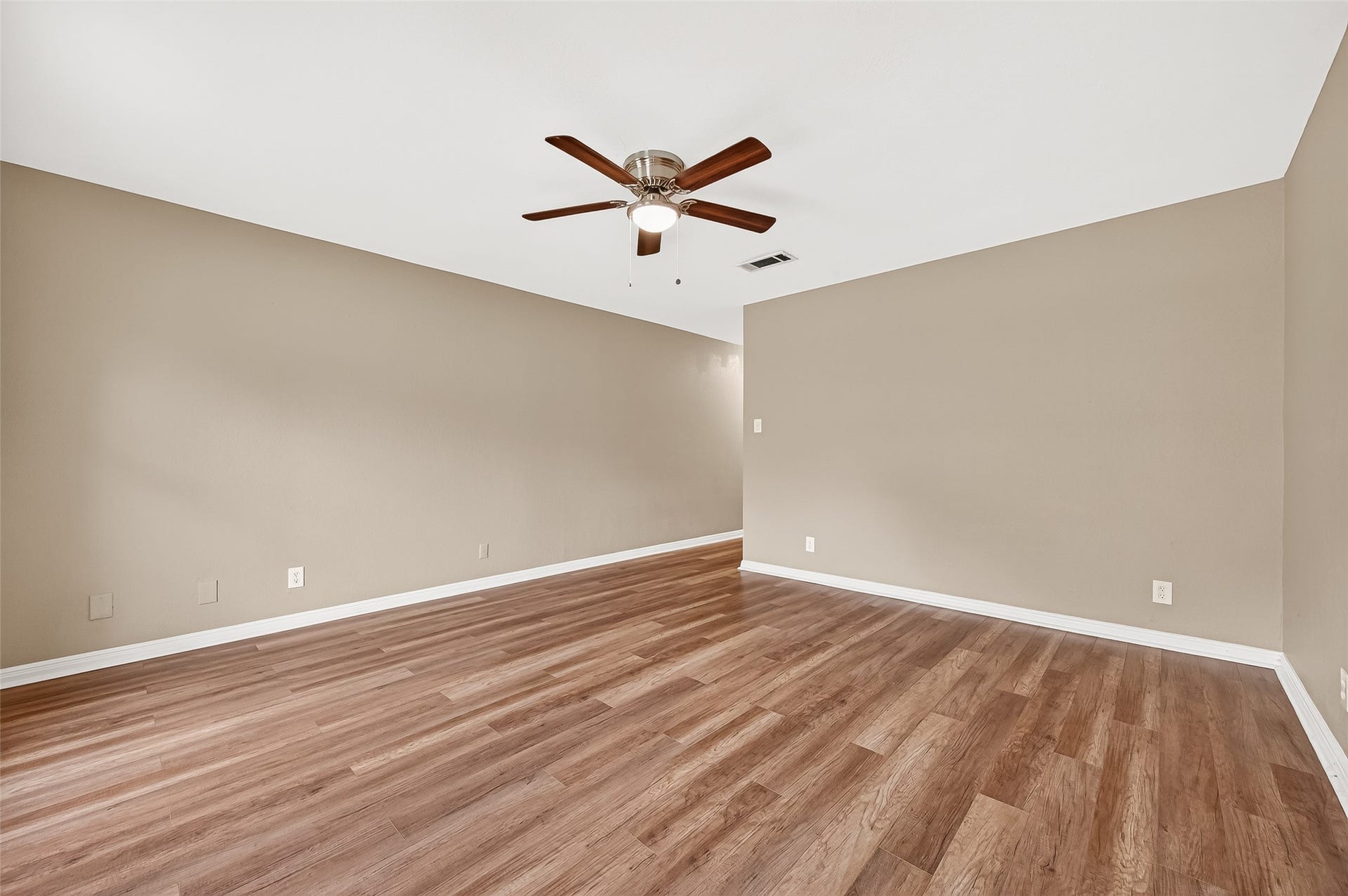 5607 Avenue M 1/2, Santa Fe, TX 77510 This photo showcases a spacious room with warm-toned walls and wood flooring. It features a ceiling fan and ample natural light, offering a cozy and inviting atmosphere ideal for various uses.