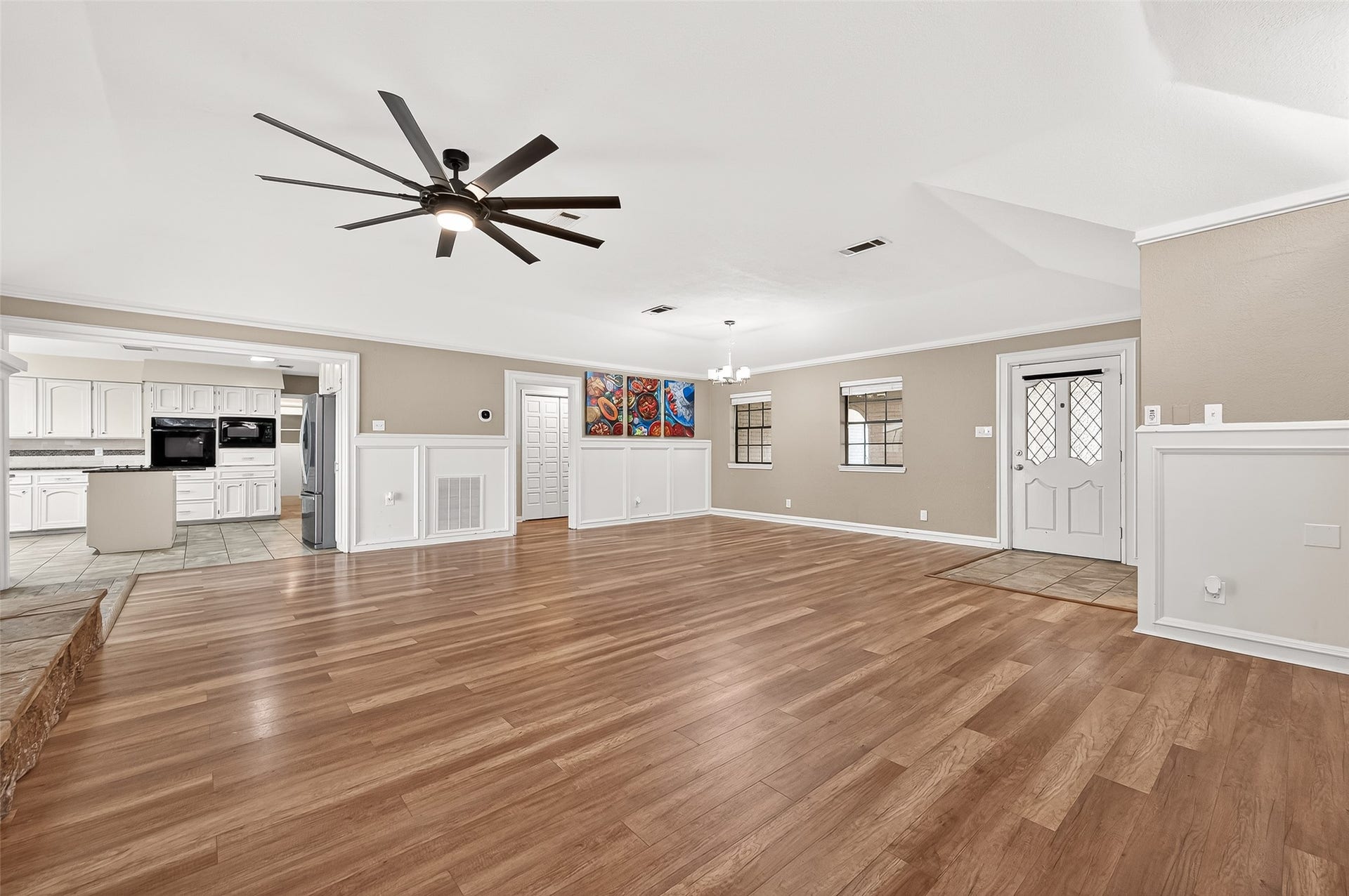 5607 Avenue M 1/2, Santa Fe, TX 77510 Living area with neutral walls. Features a modern ceiling fan and stylish wainscoting. The open layout leads to a bright kitchen with white cabinetry.